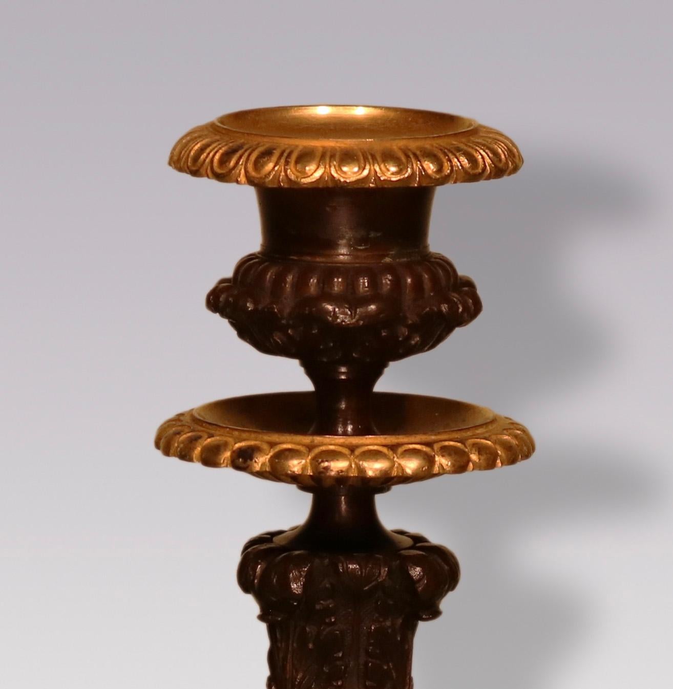A pair of early 19th Century Bronze and Ormolu candlesticks having urn shaped sconces above boldly cast bulbous stems, raised on triple Lions paw feet ending on triform bases.