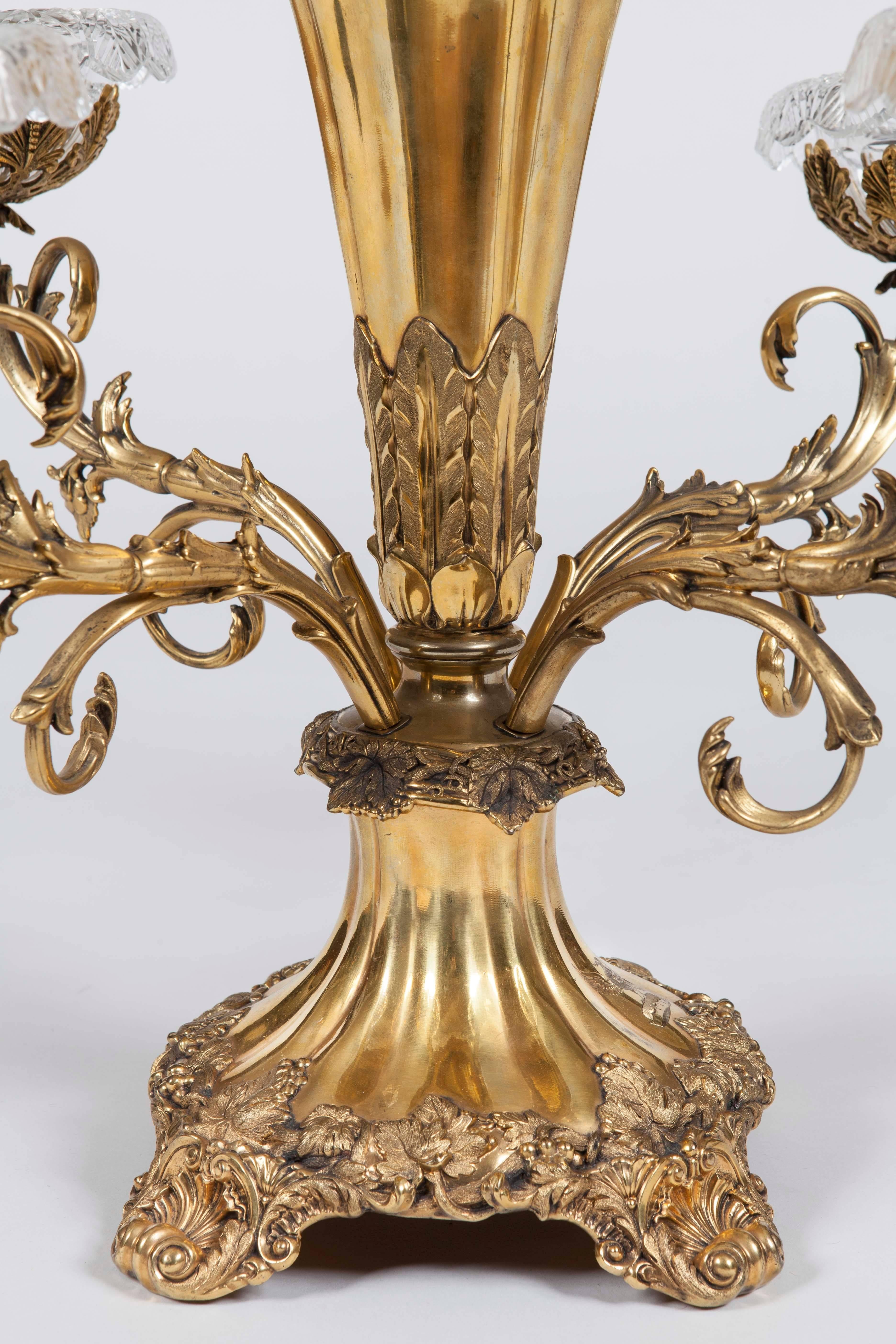 A pair of Victorian silver gilt plated epergnes
Each rising from quadripartite scallop feet, the bodies dressed with fruiting vines and foliates, issuing four scrolled and removable arms holding cut lead crystal bowls with lobed rims, framing the