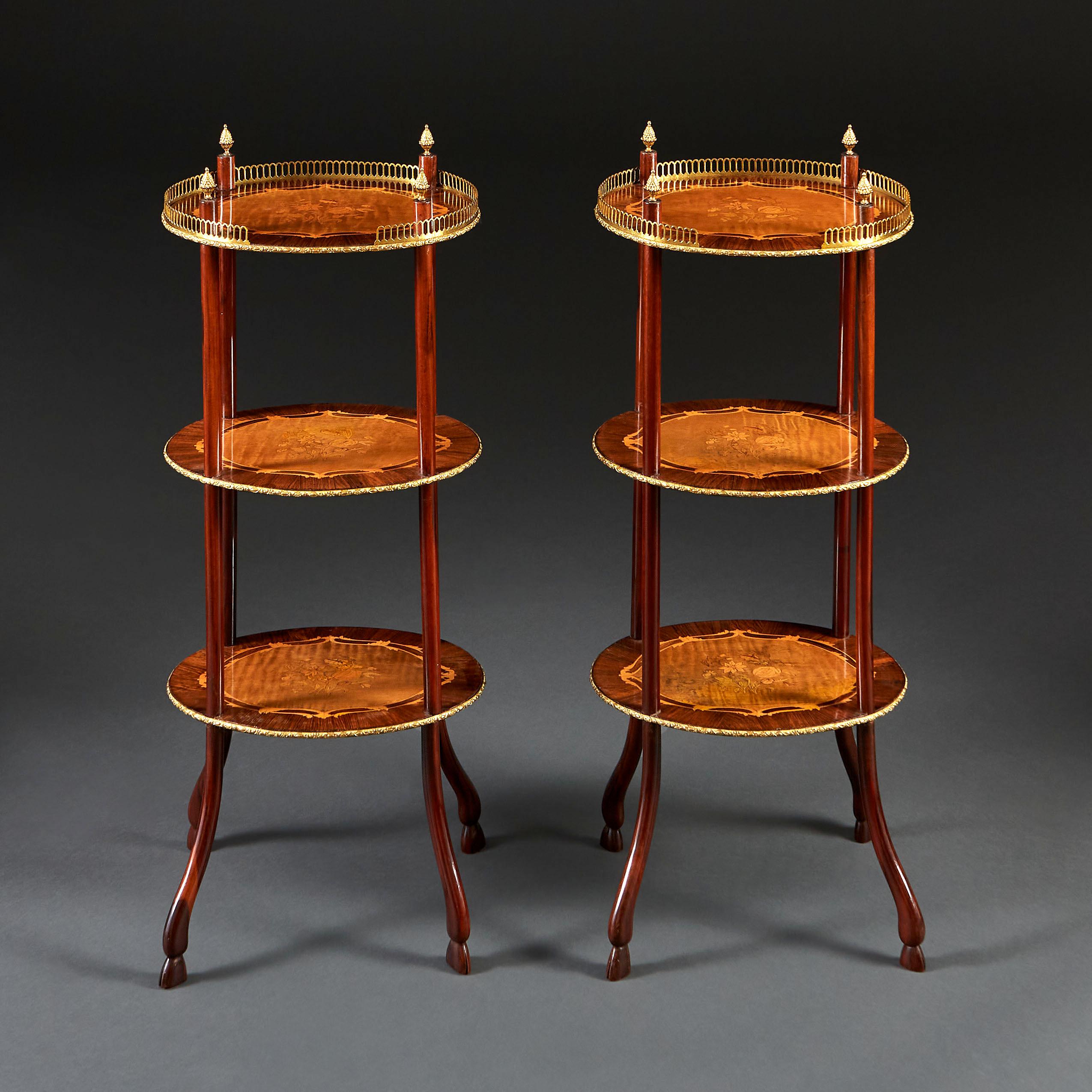 A fine pair of mid nineteenth century three tier étagères with marquetry tops and brass galleries, the uprights surmounted by brass acorn finials, and terminating in hoof feet.