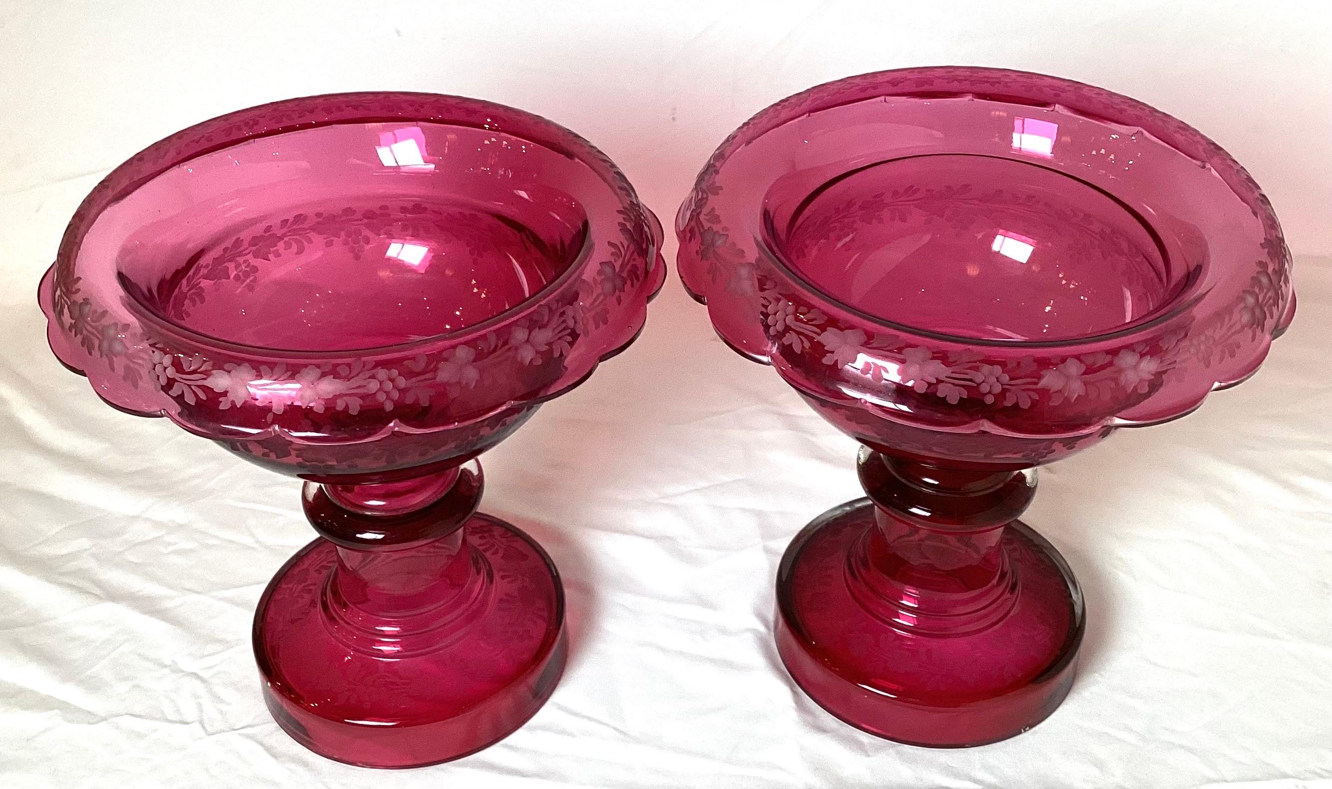 A pair of 19th century hand blown cranberry glass rolled edge footed bowl form compotes. The glass with delicate engraved grape and vine decoration.
