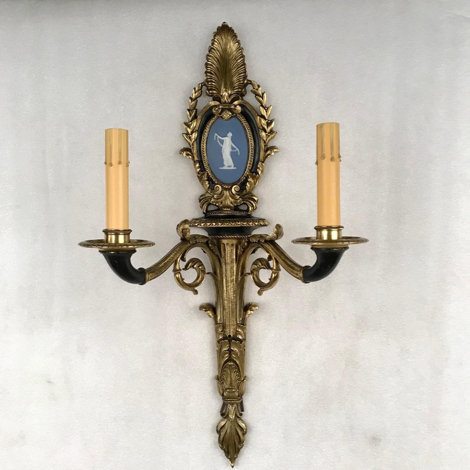 This elegant pair is in the style of the First Empire. Each is cast with palmettes, acanthus, garlands and an oval frame containing a blue bisque figure of a dancing maiden. The frame and sconces are partially ebonised giving a very Empirish feel.