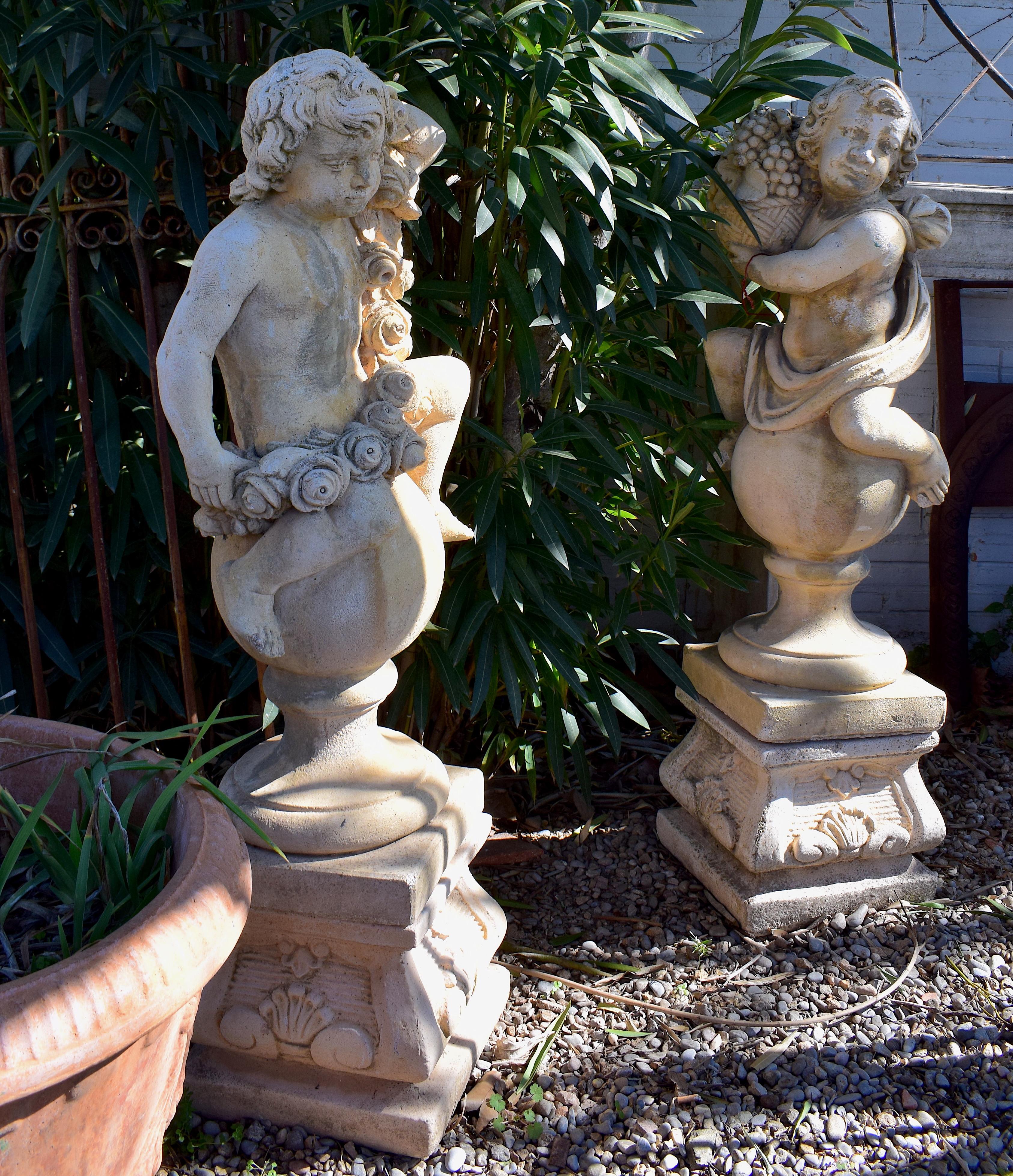 A pair of cherubs stood on plinths, these heavy jardinieres are in a good condition. They have beautiful detail and are classical designed garden ornaments. One cherub is holding grapes whilst the second is clutching a bunch of flowers. The cherub