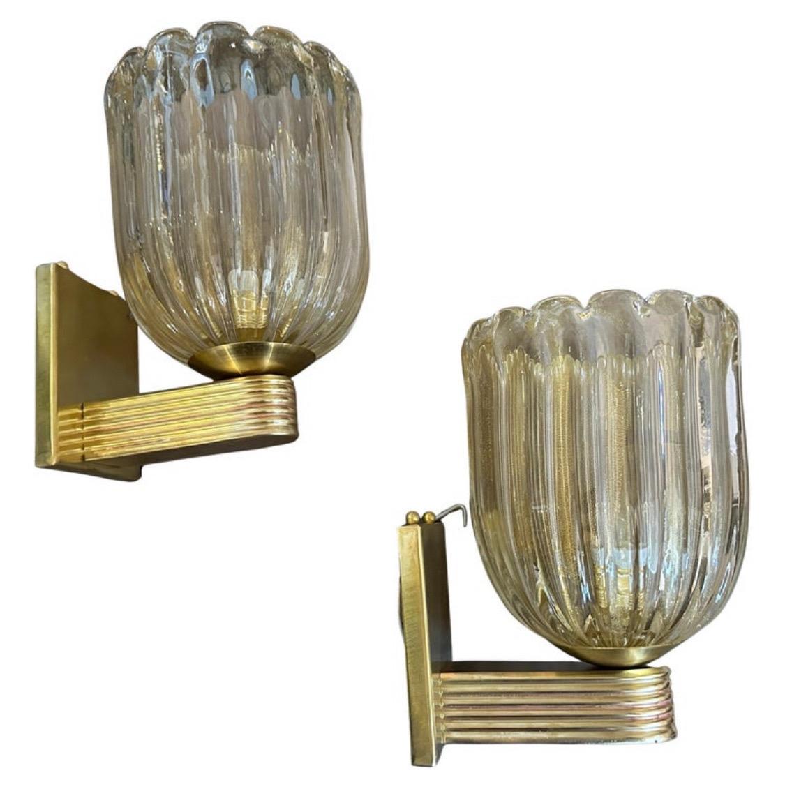 These two 21st-century gold and clear Murano glass wall sconces showcase a refined Art Deco aesthetic inspired by the Barovier style. The handblown glass shades have a delicate ribbed texture with a slightly fluted, organic tulip-like shape. The