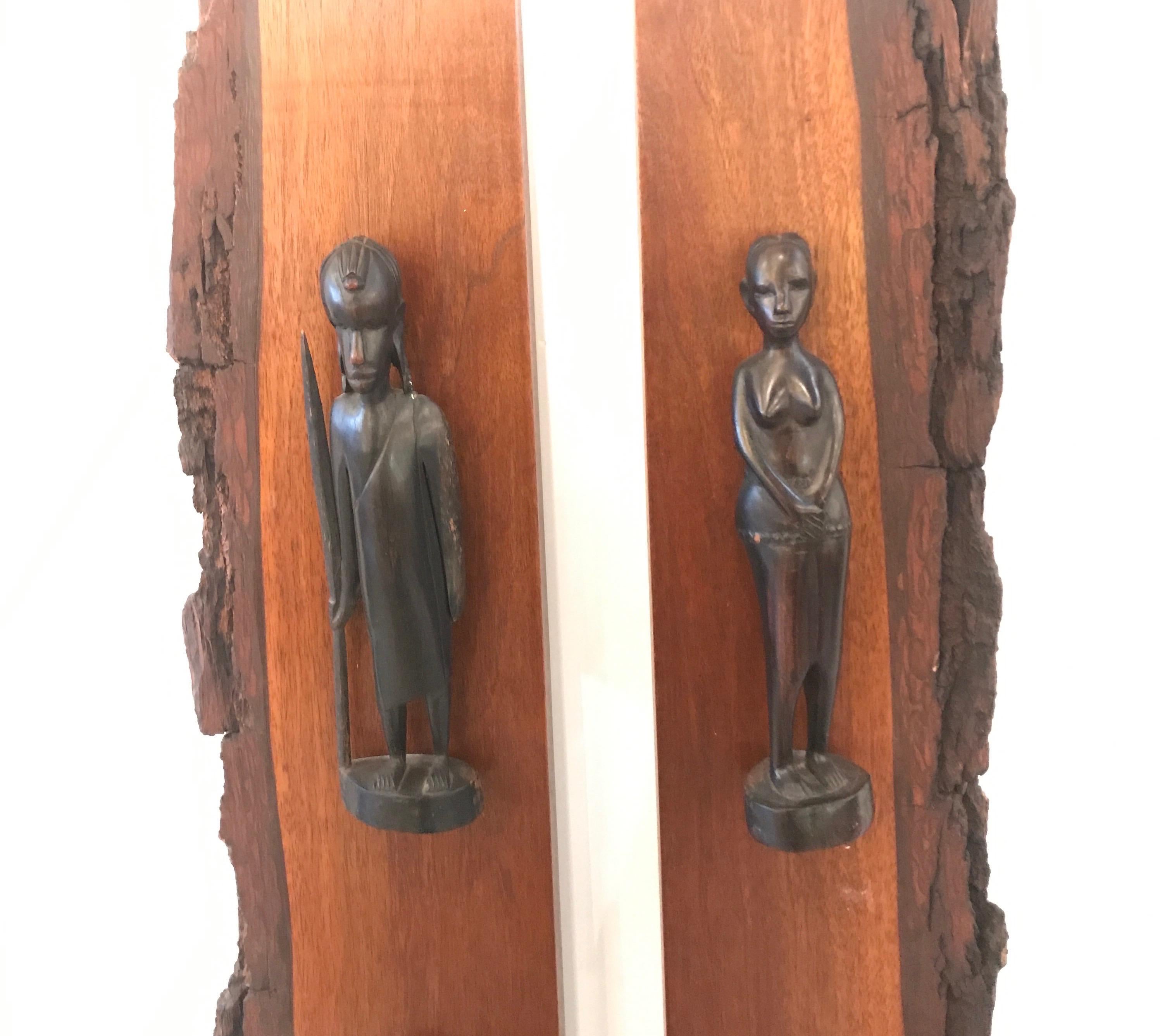 A pair of exotic hard wood panels with hand carved wood tribal male and female figures. Each panel with three hand carvings spaced evenly on the panels, mid-20th century. 53.5 inches tall.