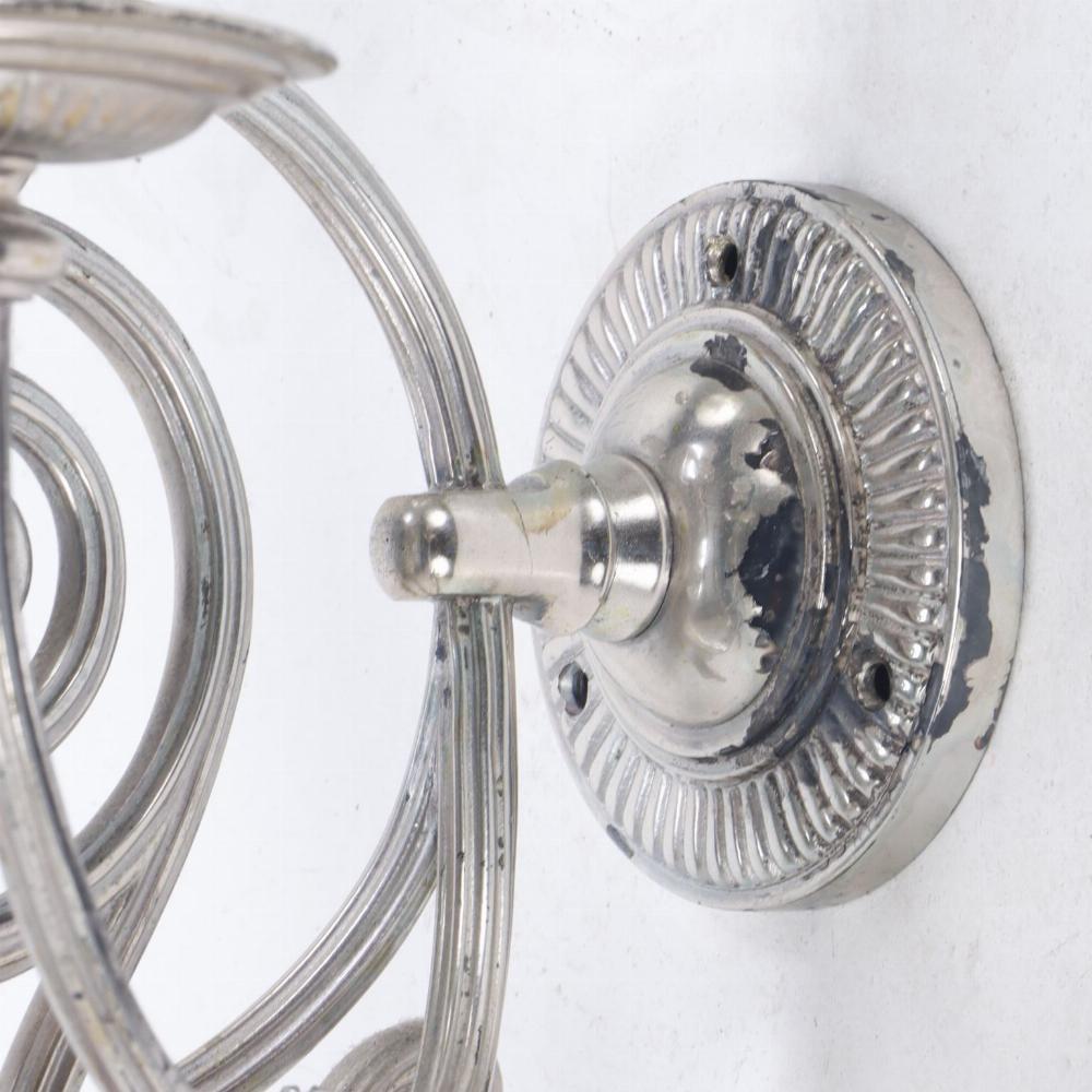 Each fixture with three scrolling arms supporting a single candle cup, all joined by a circular lobed backplate and with hanging ring embellishments.