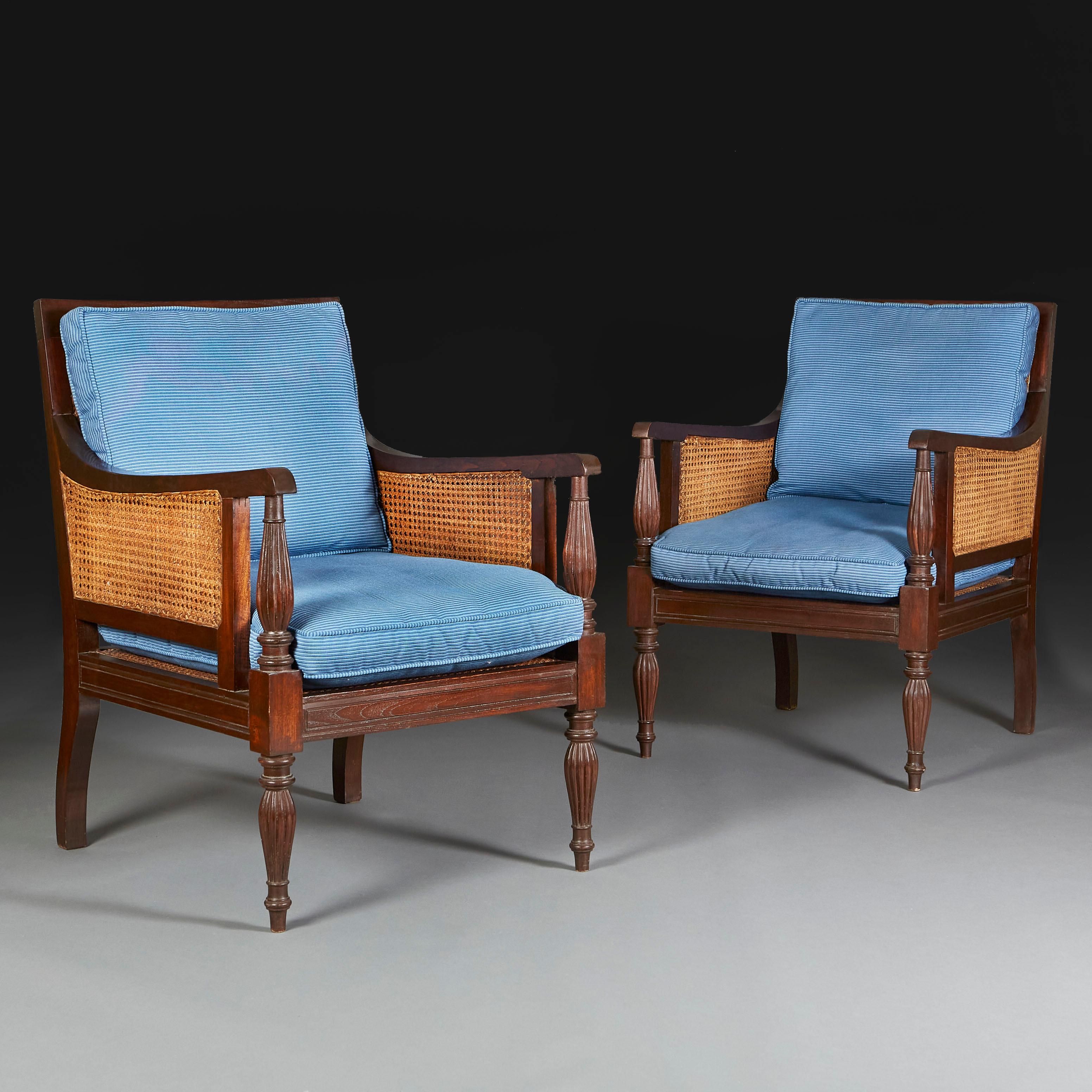 A pair of Regency style library chairs with caned seat and back, with carved arms and turned and gadrooned legs. With seat and back cushions uphlstered in blue corduroy.