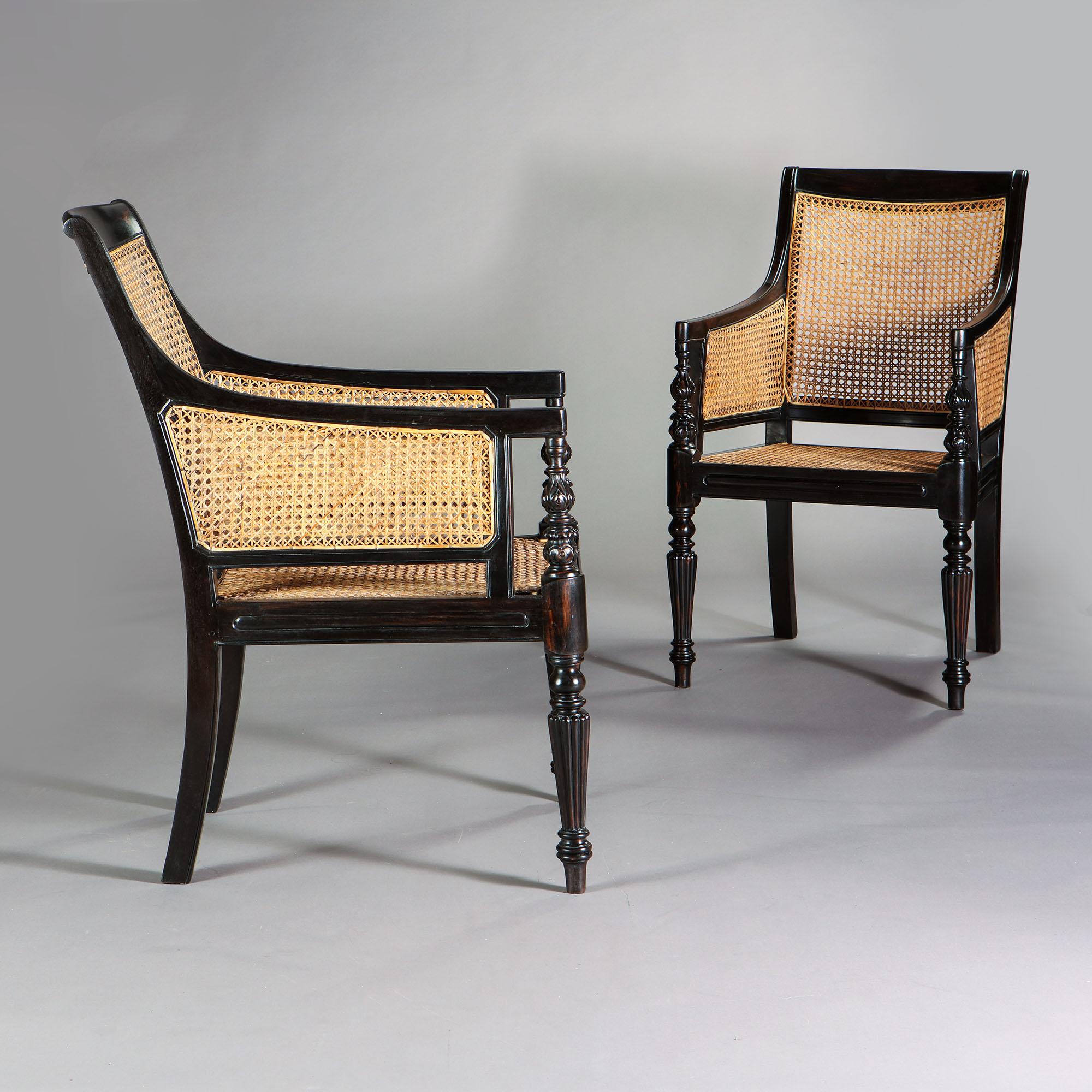 A pair of Regency style ebony library chairs with caned seat and back, with carved arms and turned and gadrooned legs.