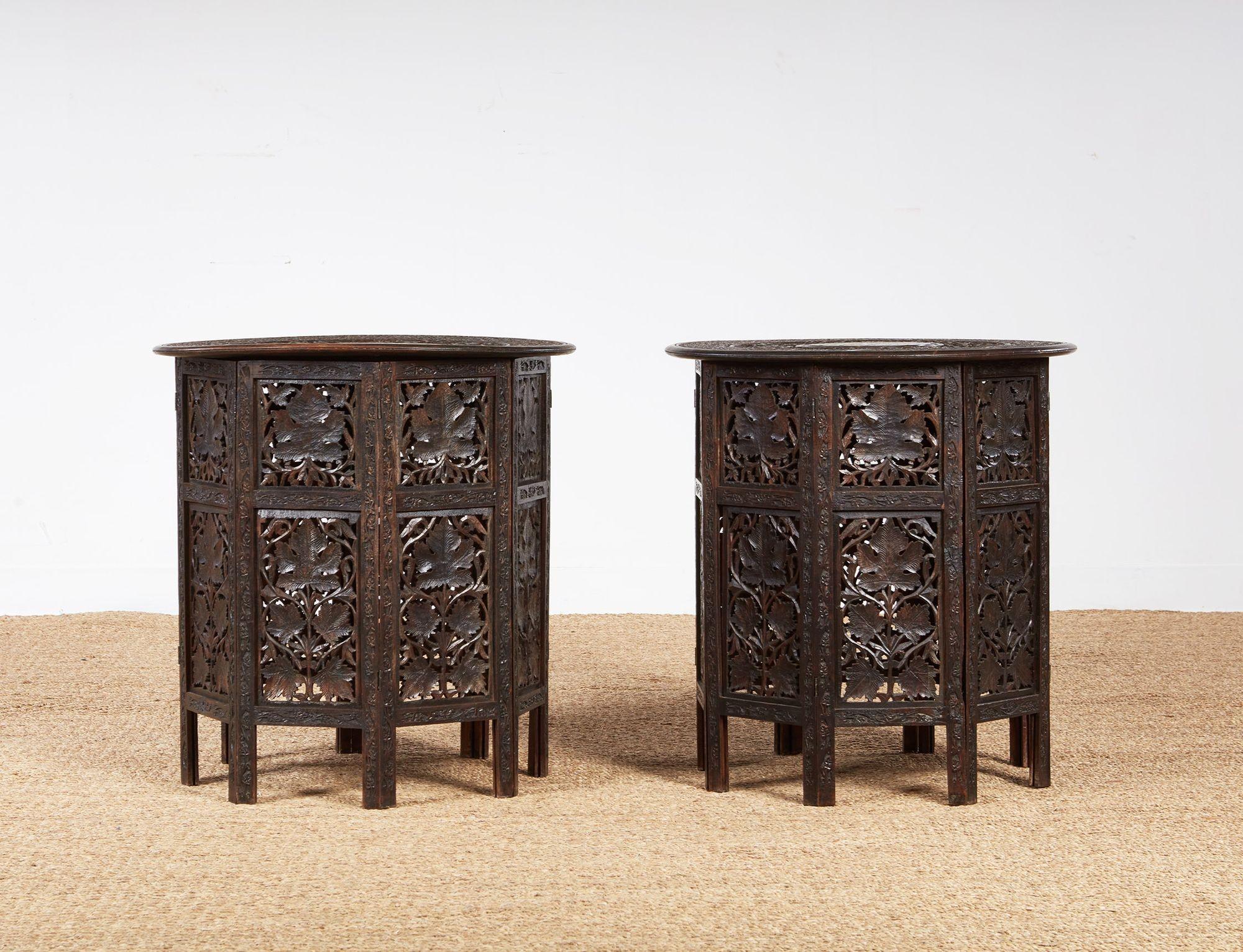 A pair of Anglo-Indian hardwood tables with round tops intricately carved with two rings of foliate and grapevine decoration and central bone inlaid medallions with a contrasting lighter ground, on octagonal bases with intricate pierced carving. 