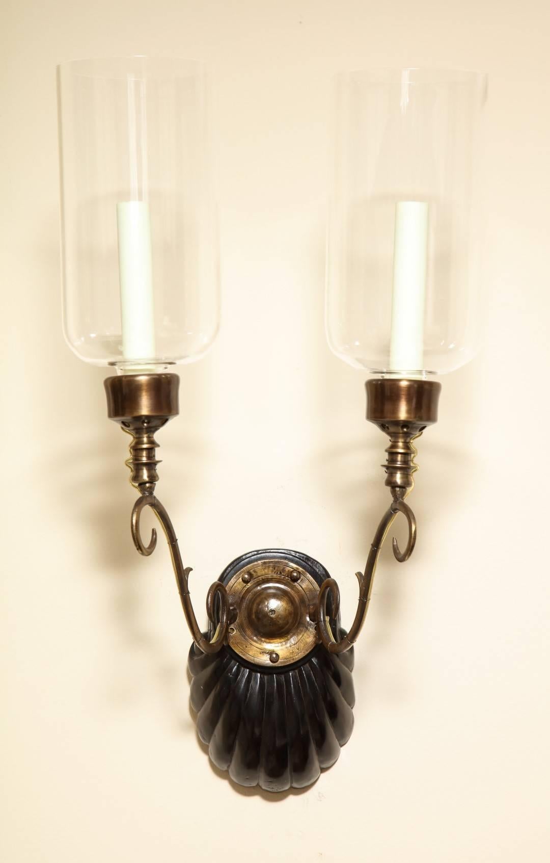 A Pair of Anglo-Indian two-light sconces, the shell form backplate issuing bronze out-scrolled candlearms supporting a single Edison socket with hurricane shade, circa 1890.
Provenance- These sconces were purchased by Albert Nestle in India, circa
