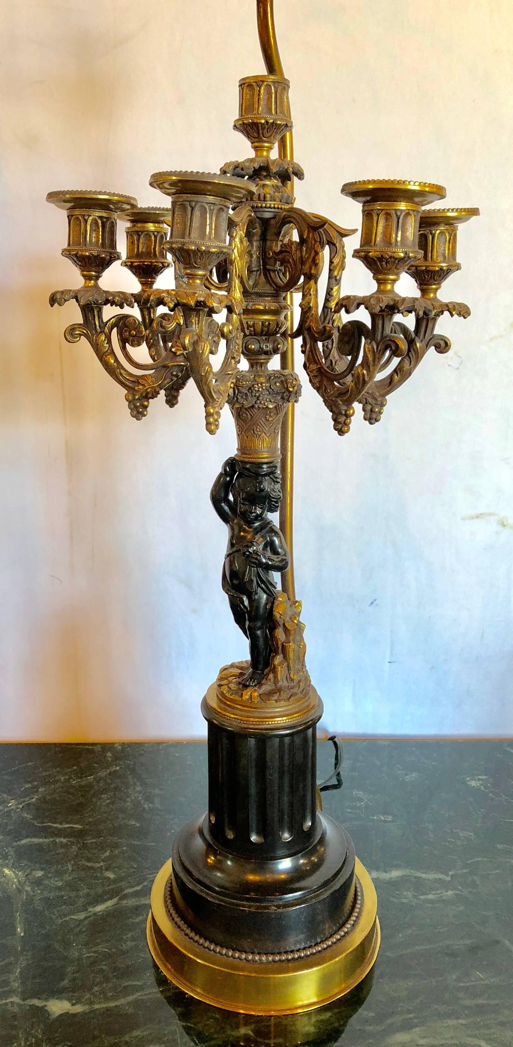 A pair of antique late 19th century bronze patinated cherub candelabras on black marble vases and dore tops and bottoms having custom shades. The cherub measuring 6.5