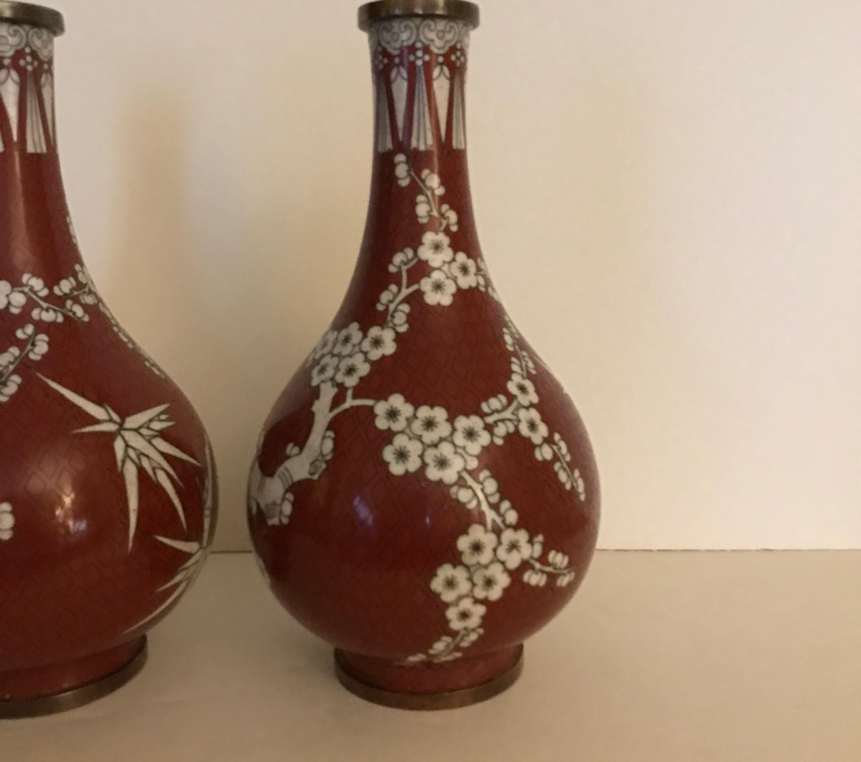 Paire de vases en cloisonné de Chine de couleur cinabre et blanc. La forme du Gordes avec un cou effilé et un corps bulbeux. Le motif est une fleur de cerisier avec des branches de bambou.... Antiquité chinoise, vers 1900.