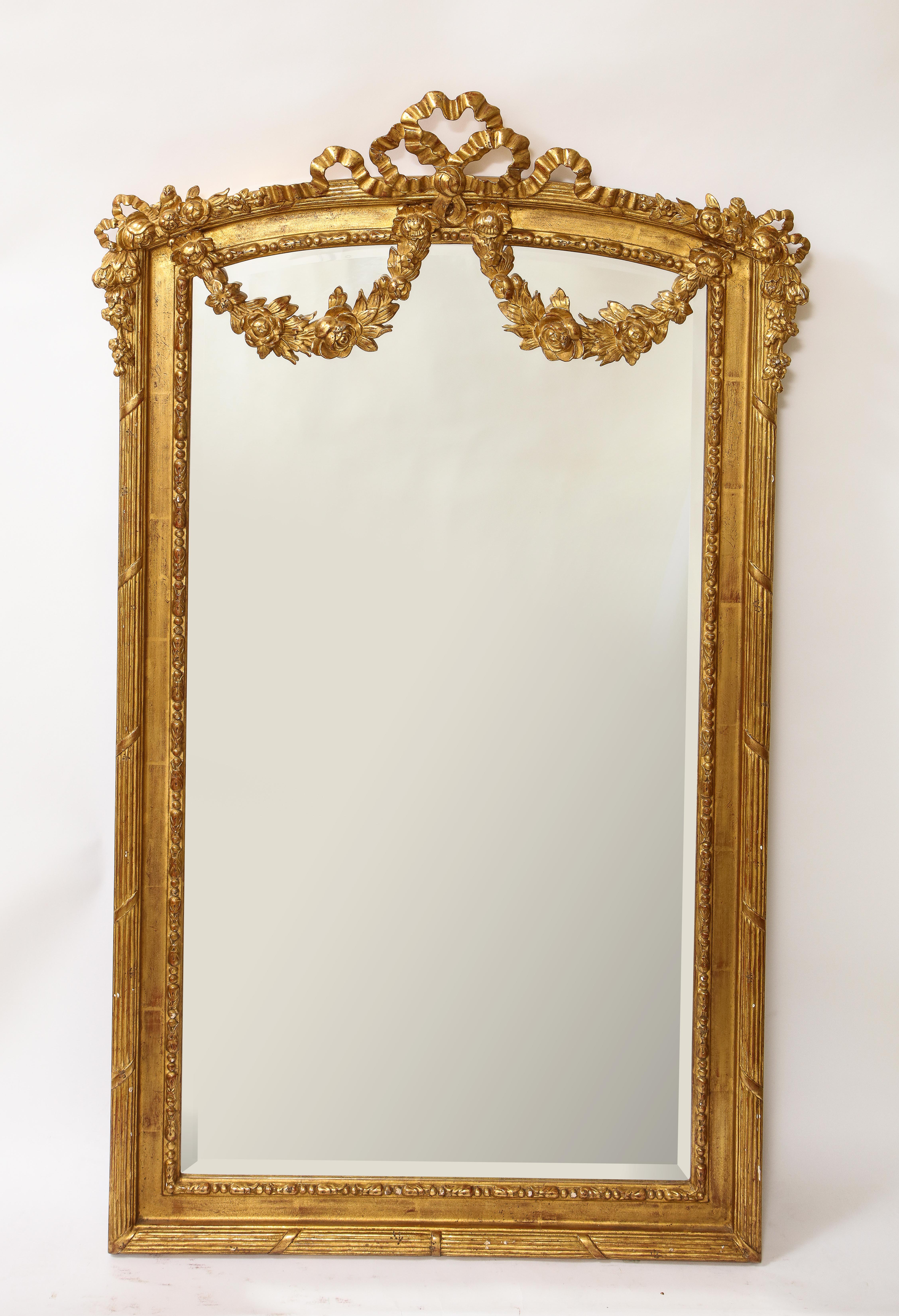 A fabulous pair of antique French Louis XVI style hand carved giltwood mirrors. Each is beautifully modeled in hand carved wood with garlands and flowers of ribbons and further enhanced with 24-karat original two-tone matte and burnished water