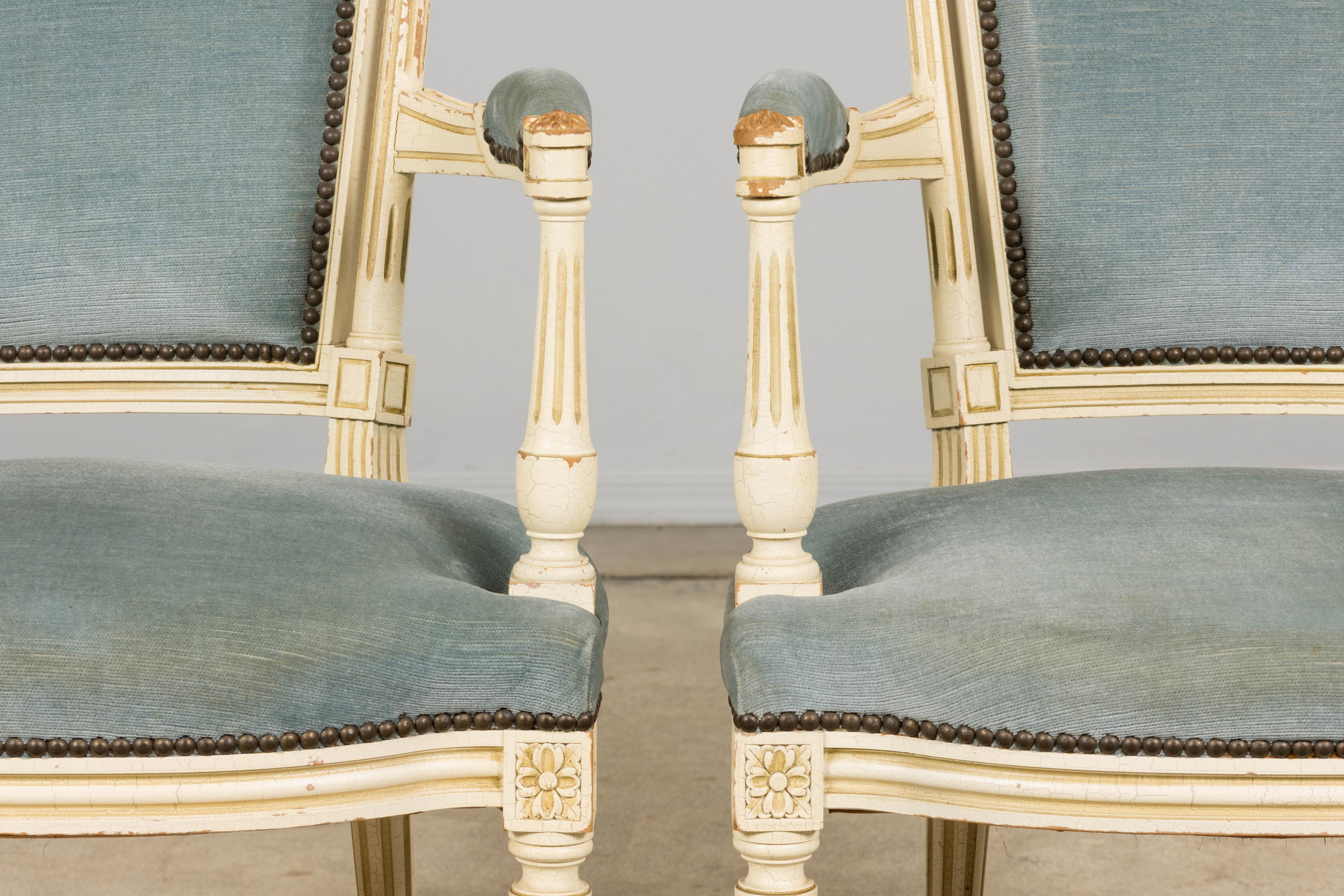 Pareja de fauteuils franceses de estilo Luis XVI / Marie Antoinette de finales del siglo XIX, tallados a mano y acabados en pintura blanca cremosa. La superficie muestra auténticos craquelados, desconchones y zonas de pérdida de pintura consistentes