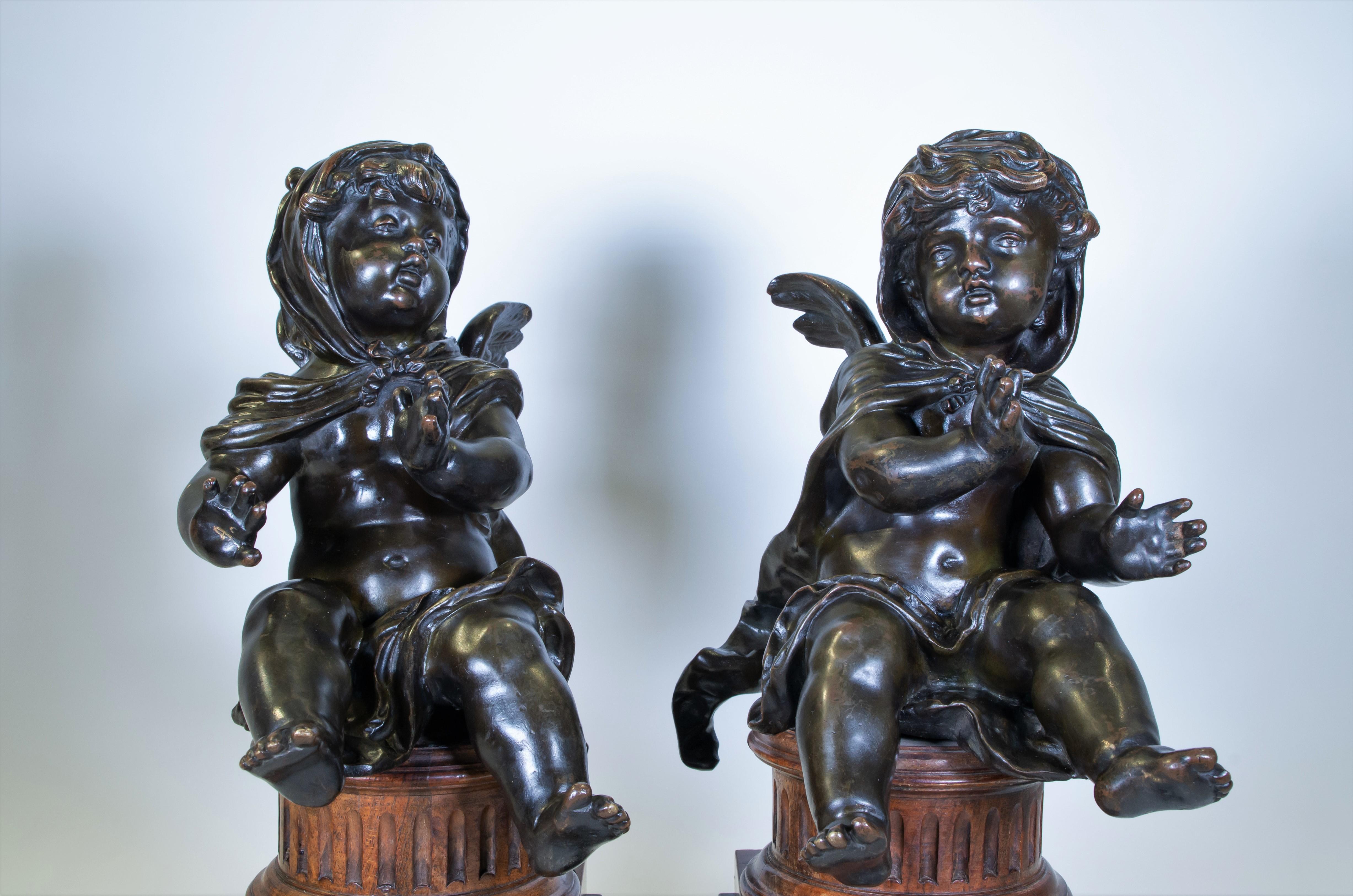 A Fabulous Pair of Antique French mid 1800s Louis XVI Style Patinated Bronze Putti Seated on Fluted Plinths. Each putti is seen seated with their arms and legs extended. They are both cloaked and winged with calming appearances. A dark brown patina