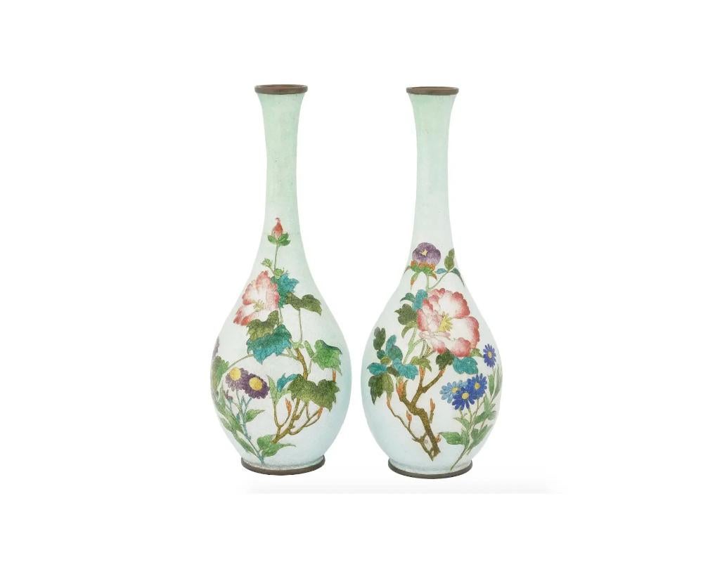 A pair of antique Japanese Meiji era Ginbari enamel vases. The ground of the vases are covered with enamel in a white shade. The vases are enameled with polychrome images of blossoming flowers made in the Cloisonne technique. Ginbari is a Japanese