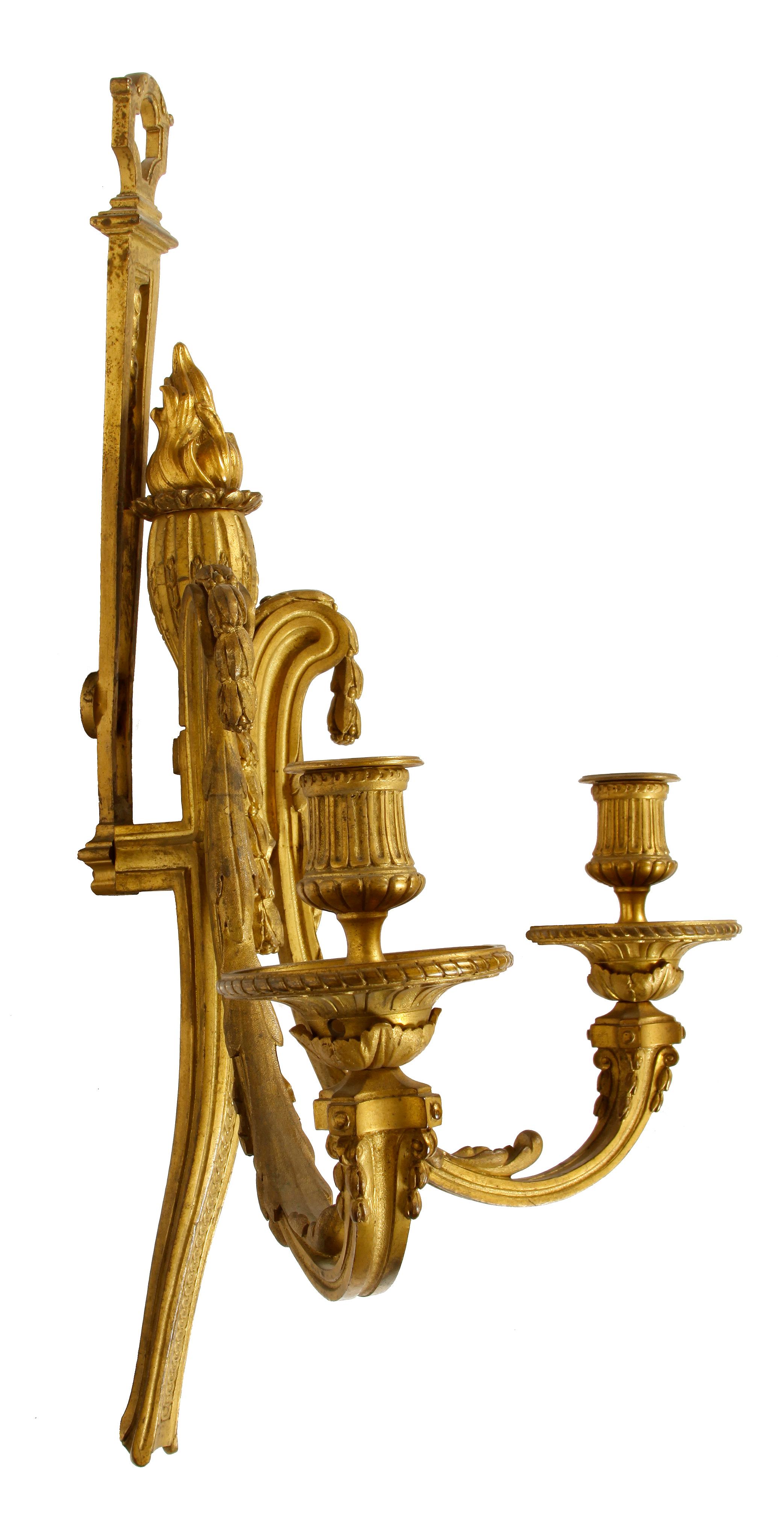 A pair of antique Louis XVI style two-arm bronze wall scones. Each arm decorated with leaf detail and depicting a torchère at the center.