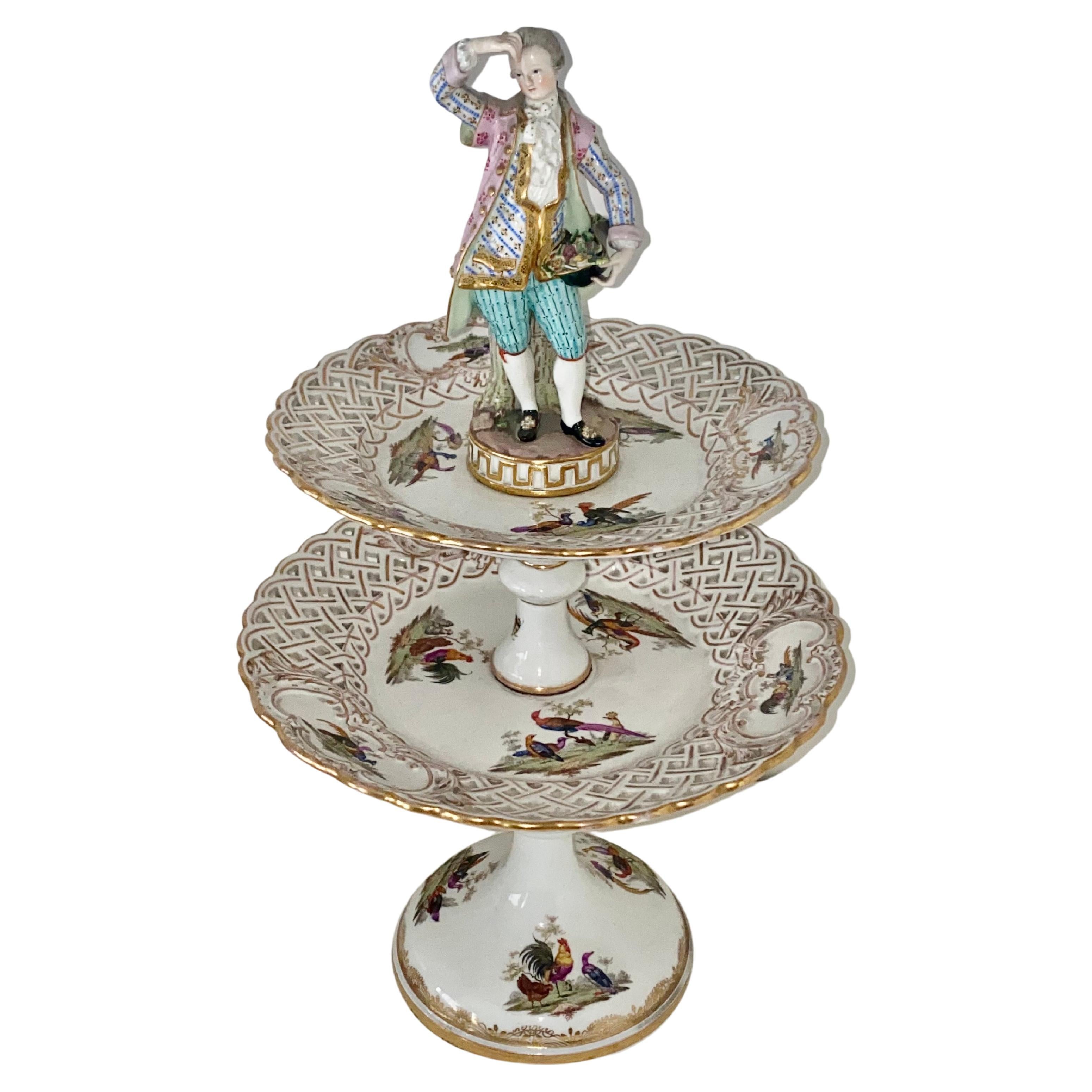 A fine quality pair of 2-tier stands with figural finials of a maiden and man. The reticulated plates and supports each painted with various types of birds, waterfowl, insects and flowers. The base is marked with the blue Meissen cross swords