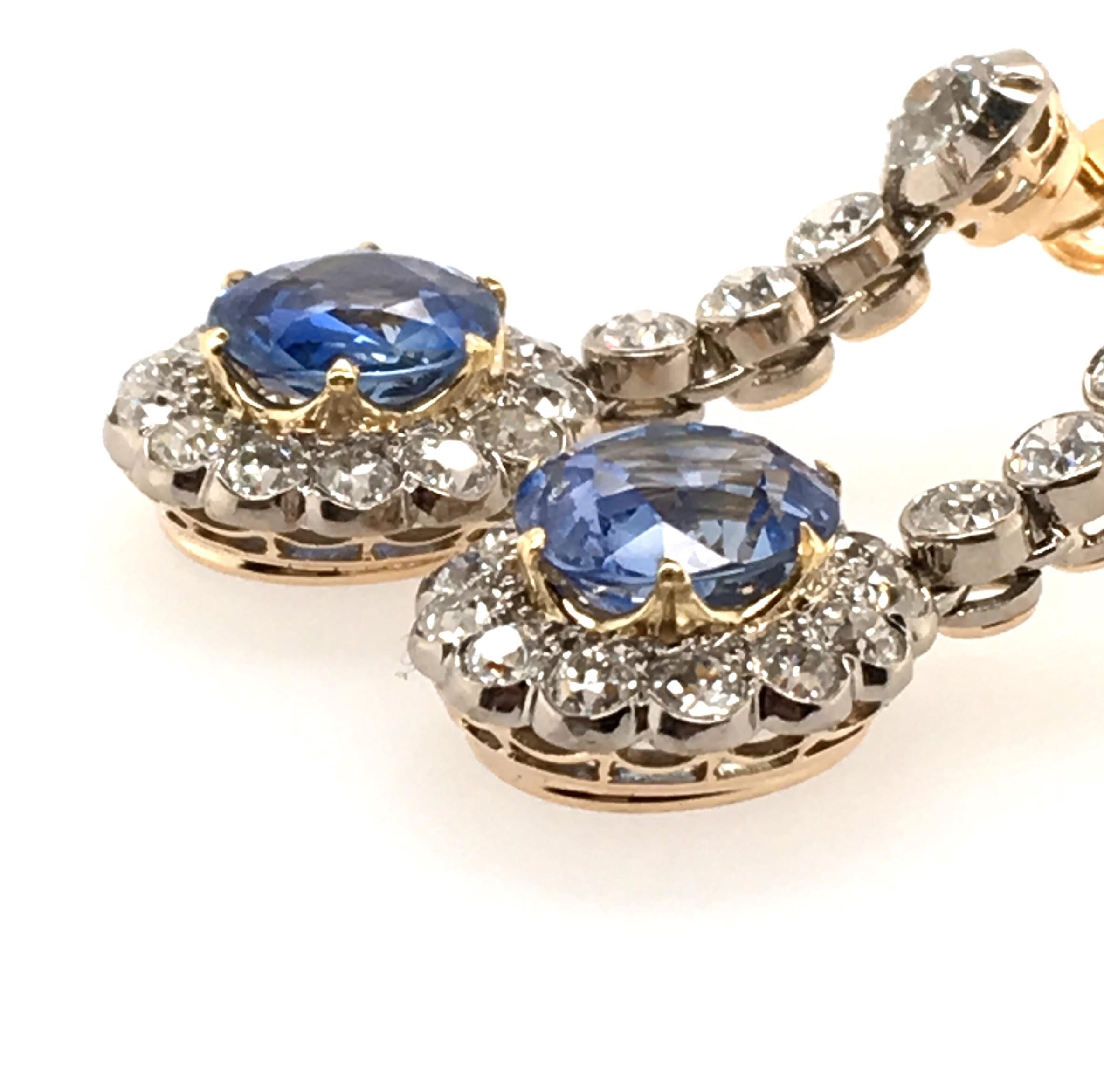 A pair antique 15 karat yellow gold, silver topped, sapphire and diamond earrings. Circa 1910. Each suspending an oval cut sapphire, weighing 5.79 carats total, within an old cut diamond surround, from an articulated line of old cut diamonds. Thirty