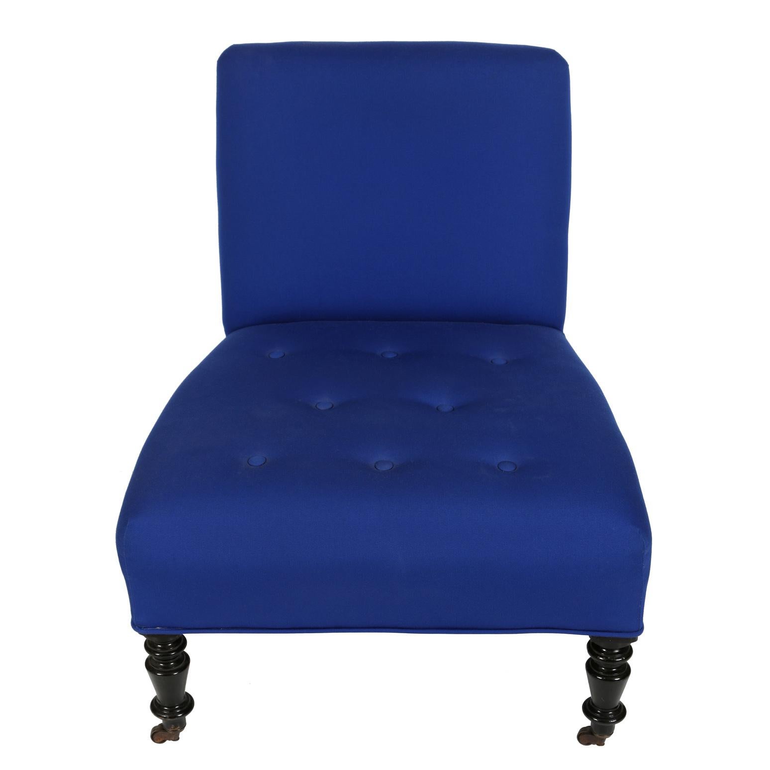 A pair of antique slipper chairs in cobalt blue fabric with tufted seat, smooth back, ebonized turned front legs and casters on all four feet.