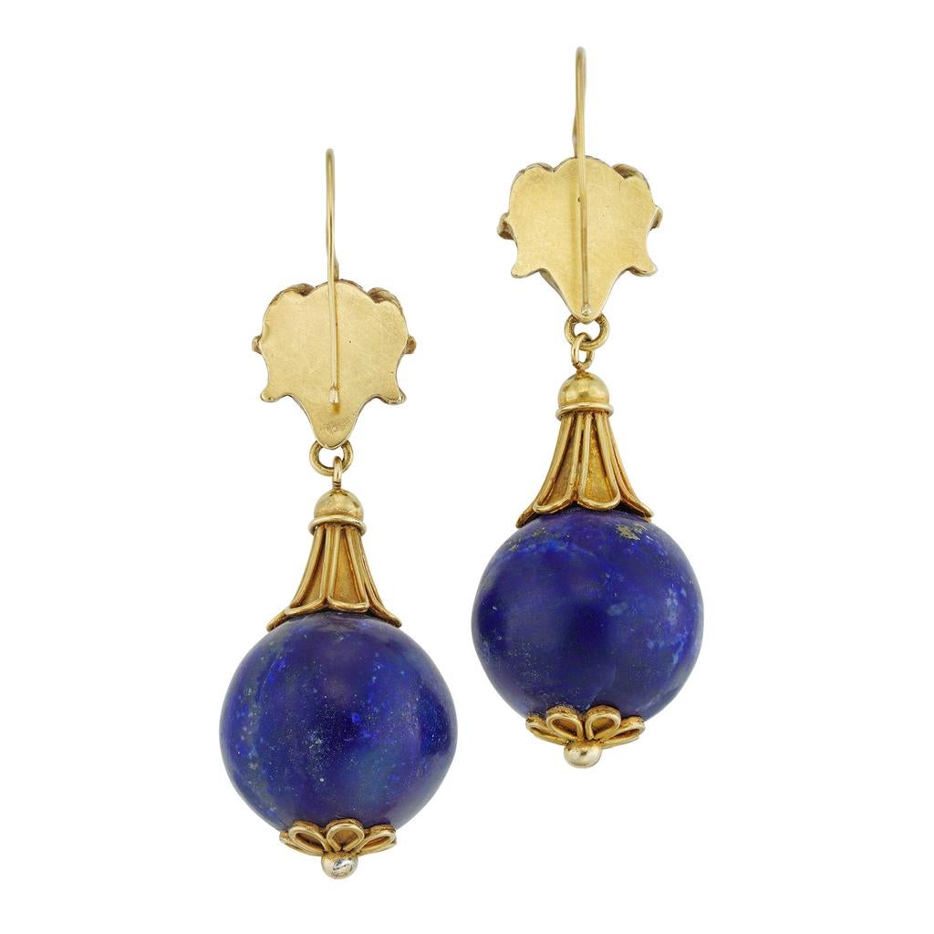 A pair of Archaeological Revival lapis and gold drop earrings, each earring with a realistically carved ram’s head, suspending a spherical lapis bead at the top with a conical gold cap of fluted design and at the bottom bearing a gold anthemion