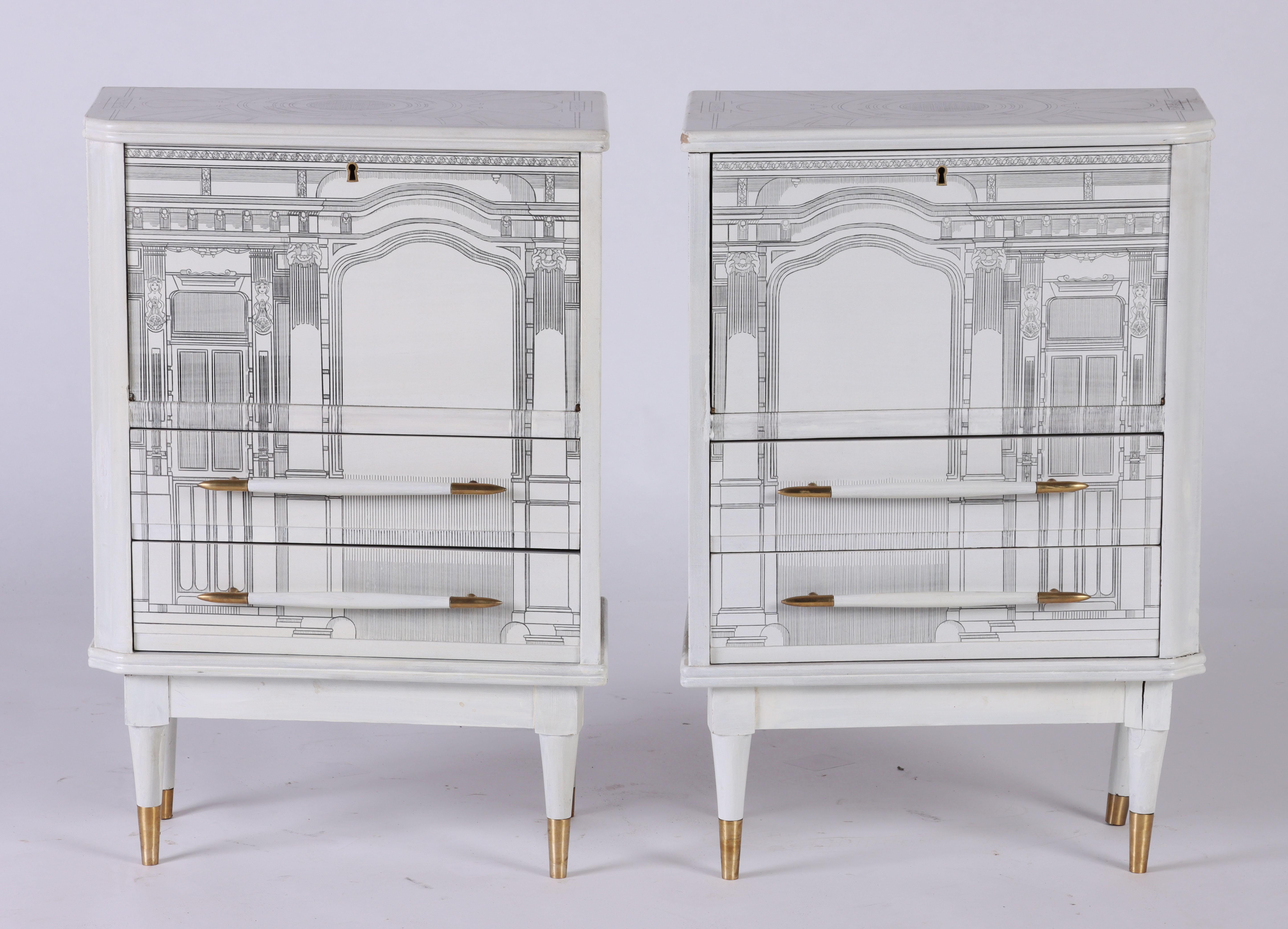A pair of architectural small cabinets decorated in the manner of Fornasetti. White painted with brass details. Circa 1960.