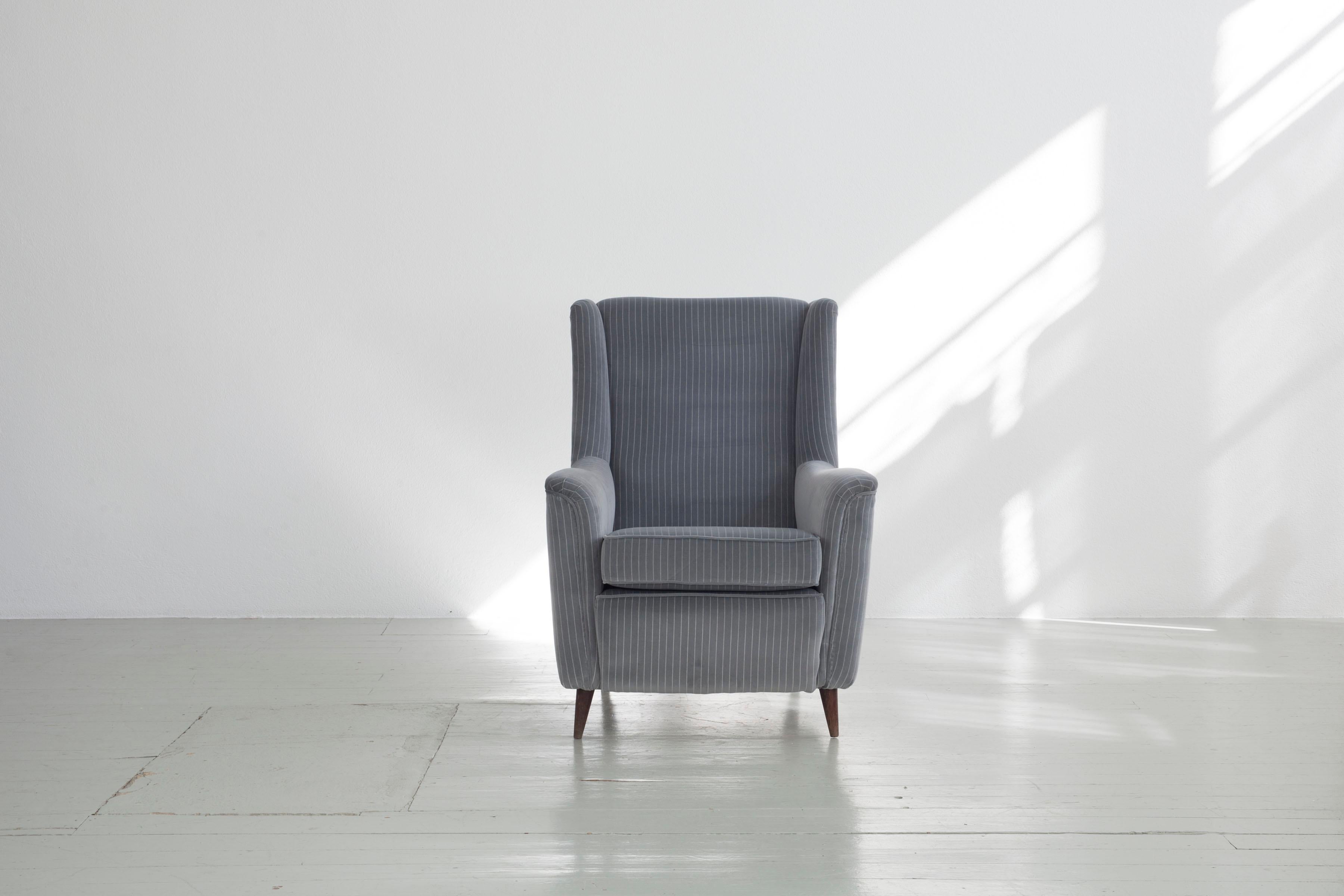 This Italian pair of armchairs was designed by Ico Parisi and manufactured by Ariberto Colombo in Cantu in the 1950s. The piece of furniture is upholstered in a grey and white striped velvet fabric, is supported by dark wooden legs and is in good