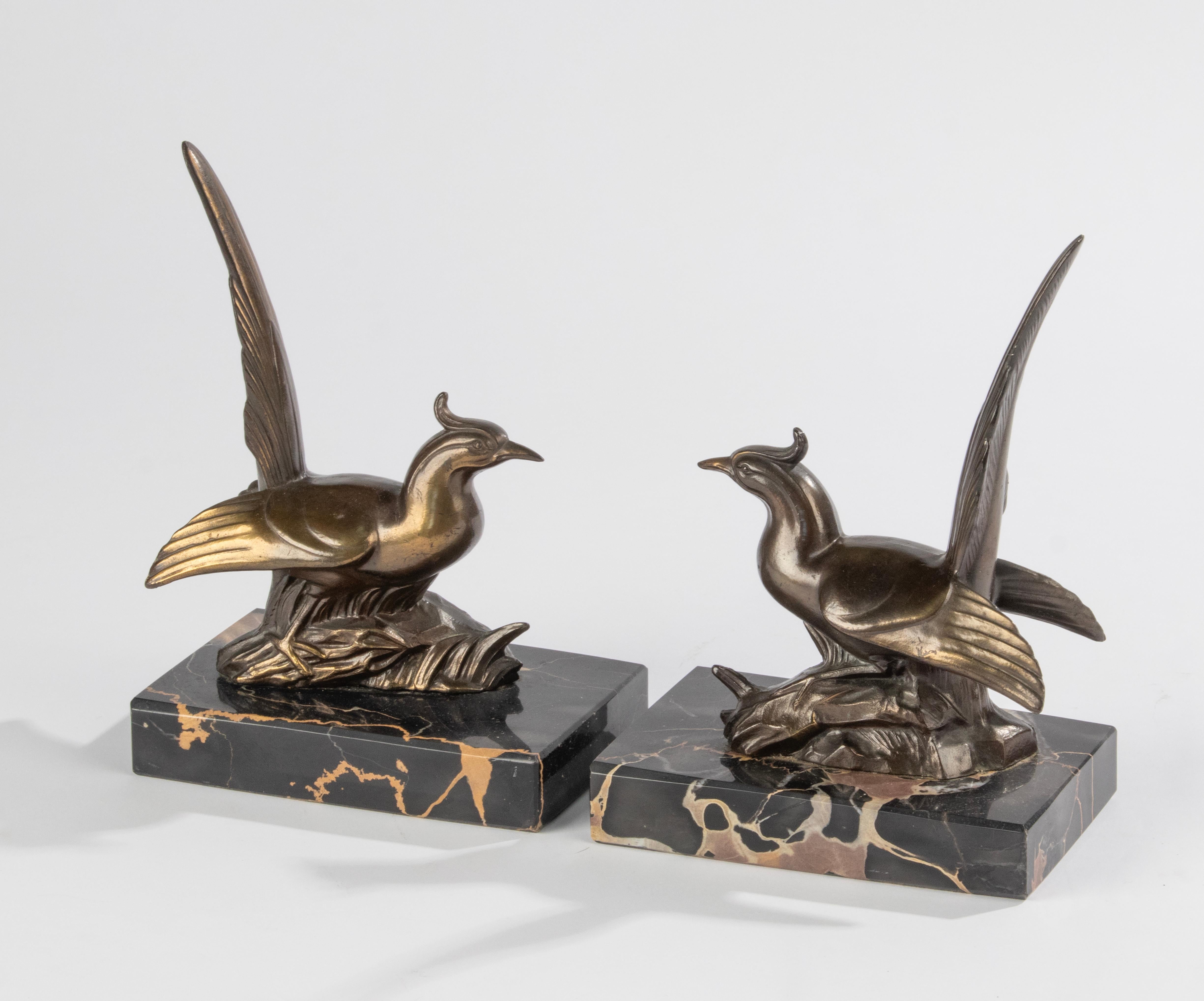 Ein Paar Buchstützen aus der Zeit des Art déco, mit Skulpturen von Fasanenvögeln. Die Figuren sind aus bronzefarben patiniertem Zinn (Zinklegierung) gefertigt. Die Sockel sind aus Porto Nero Marmor gefertigt. Alles in gutem Zustand. Hergestellt in