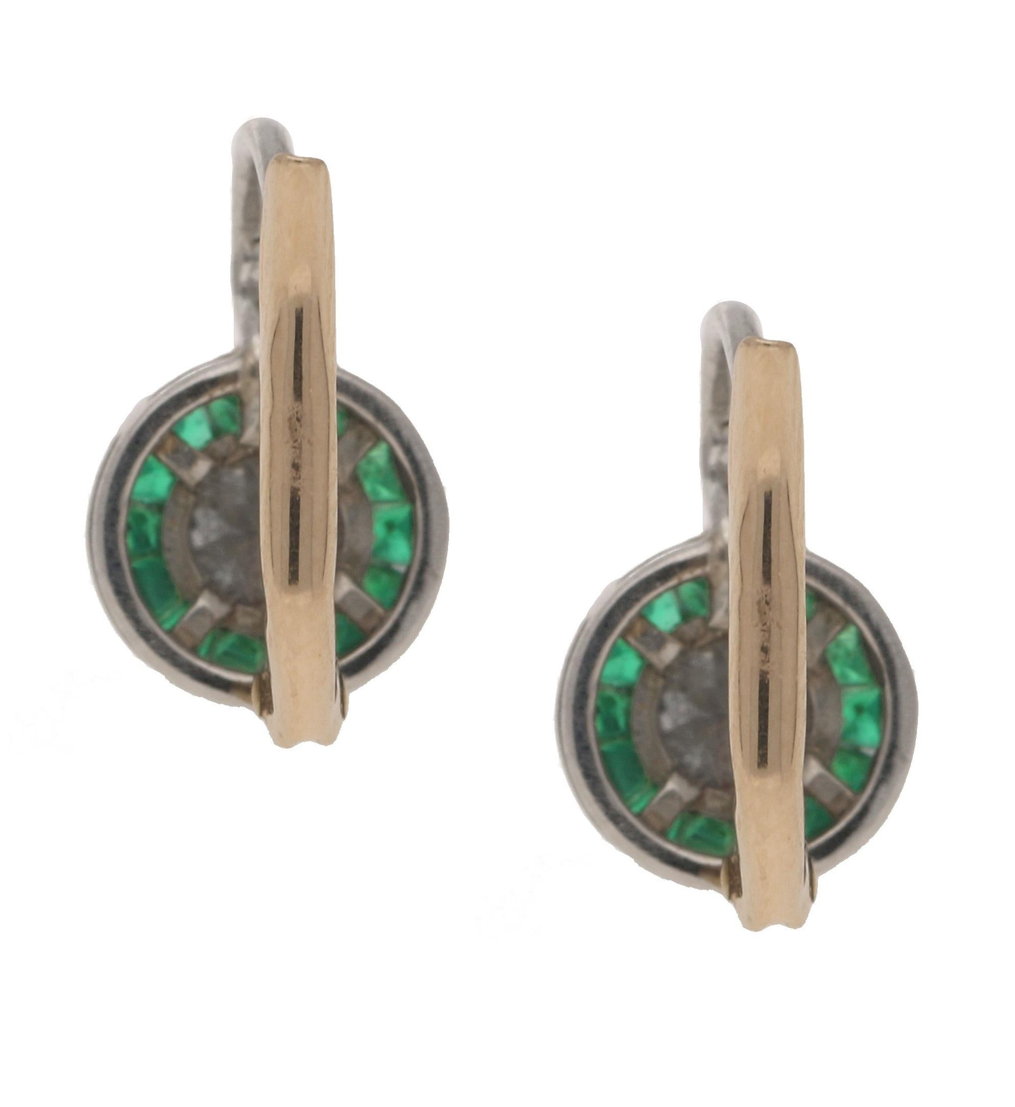 A pair of Art Deco styled diamond and emerald target earrings in 18-karat white and rose gold, each earring featuring an Old European brilliant-cut diamond millegrain-set to the centre, encircled by a halo of similarly-set calibre-cut emeralds, all