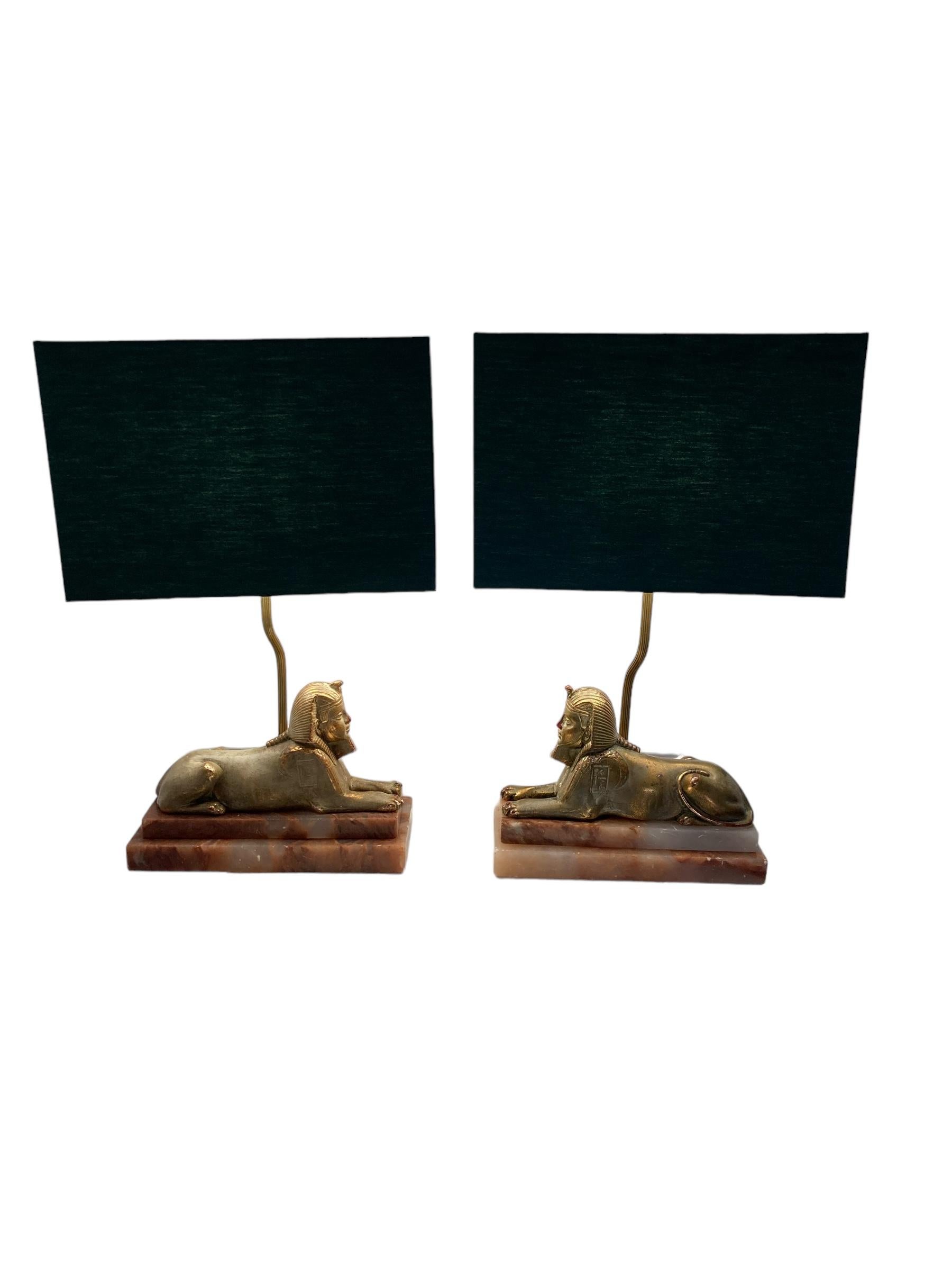 Paar Art Deco Egytian Sphinx Stil Tischlampen auf einem Marmorsockel dunkelgrüne Schirme.  Diese mit viel Liebe zum Detail gefertigte Leuchte vereint mühelos Eleganz und Stärke. Wunderschön geformt, verleiht sie jedem Raum einen Hauch von