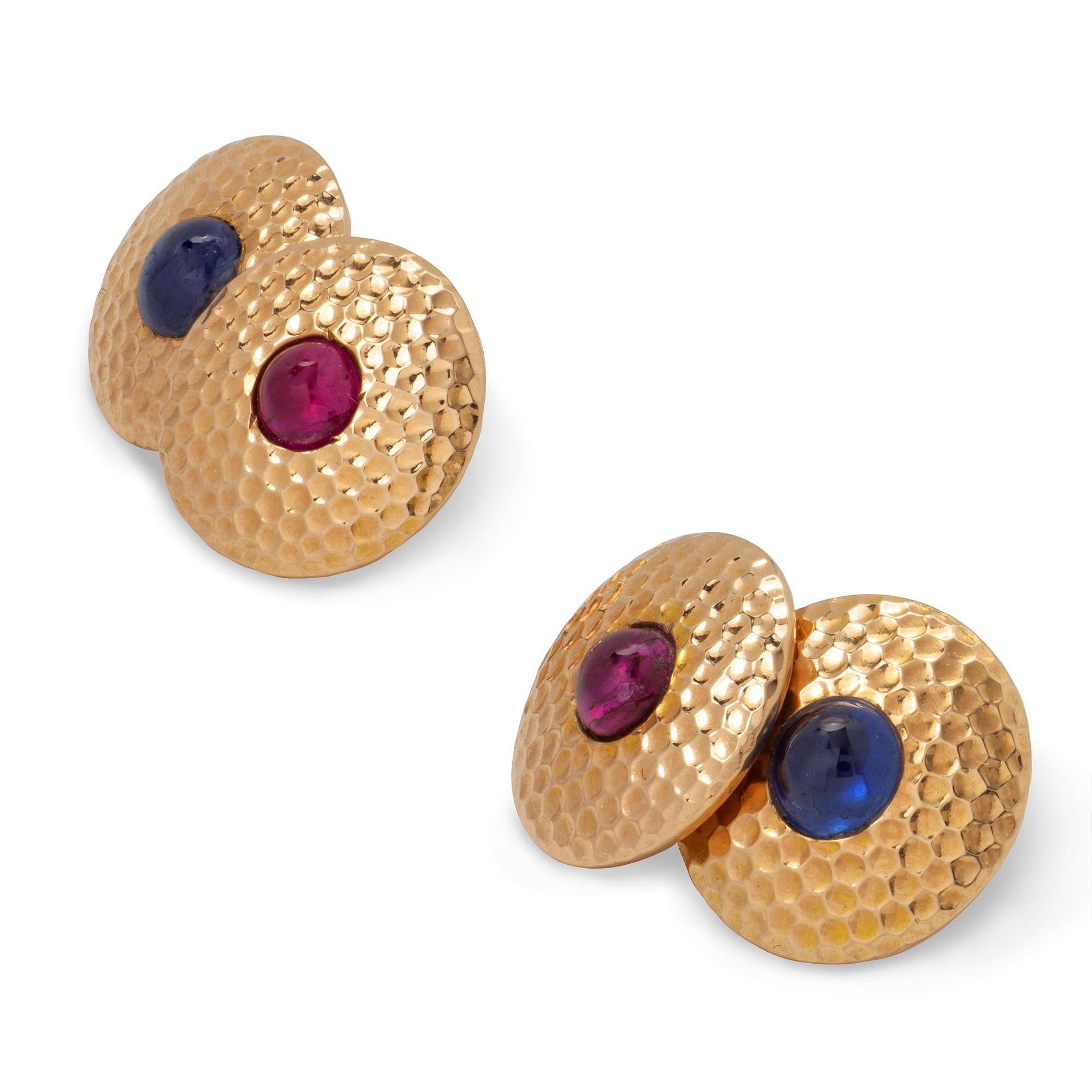A pair of Art Deco gem-set yellow gold cufflinks, each cufflink consisted of two round plaques of hammered gold, the one set with a cabochon ruby and the other with a cabochon sapphire with oval chain link, circa 1920,  measuring approximately 1.3cm