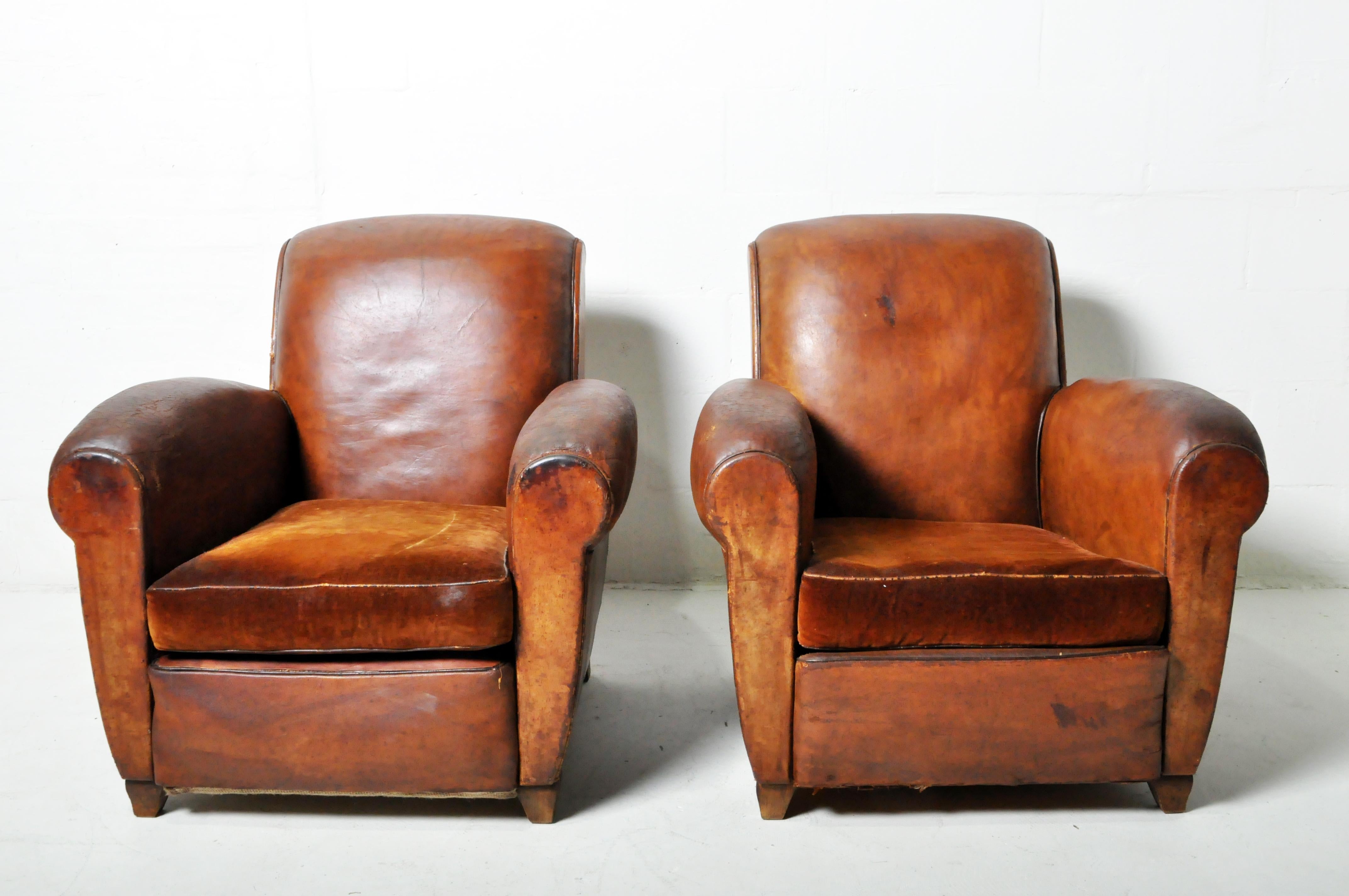 A vintage pair of French Art Deco leather club chairs with original patina. The seat cushions are vintage mohair velvet, a tasteful and expected replacement for worn-out leather cushions. The original springs have been re-tied and saved. The old