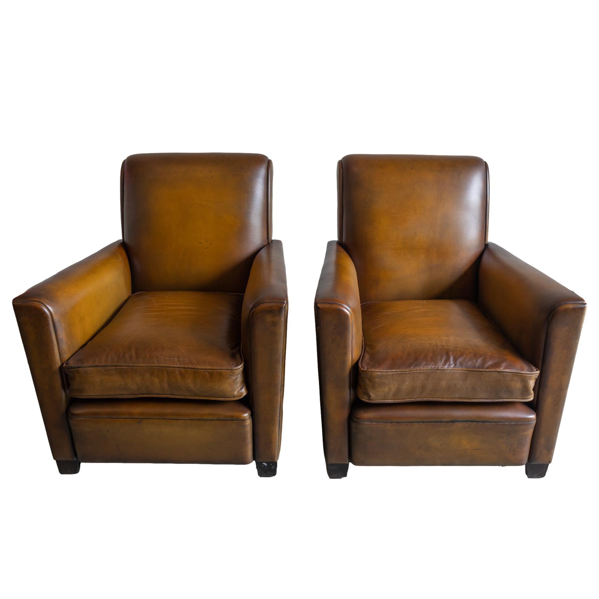 A Pair of Art Deco Leather Club Chairs of geometrical, flared form, the deeply slanted back slightly rolled, on tapered front feet, the rear feet flared, with down-filled over-stuffed cushions, French, ca. 1935.