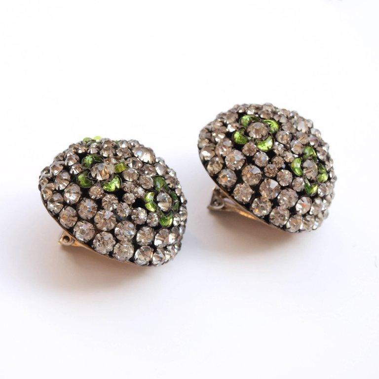 Paste diamonds and cut green glass flowers set in a pair of half sphere clip-on earrings. Costume jewelry with unmistakable 1930’s boldness of style. There is some loss to one of the earrings with damage to part of a green flower petal and the