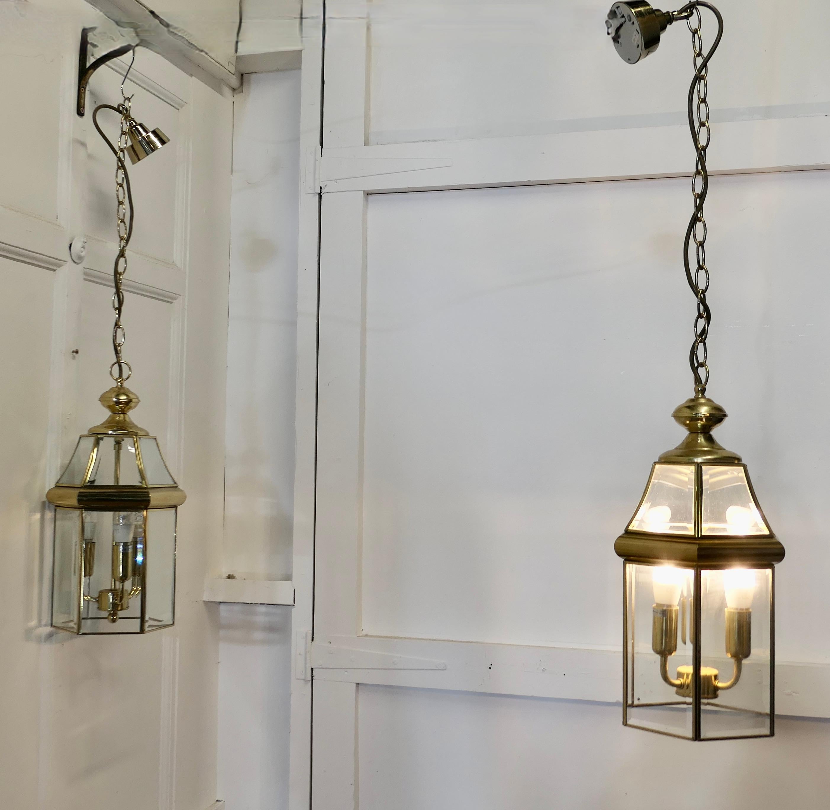A Pair of  Art Deco Style Brass & Glass Hall Lanterns

A superb impressive pair of brass lanterns, these have 6 clear glass sides set with bevelled cut glass both  high and low with 3 bulb holders inside, they each hang on a brass chain and ceiling