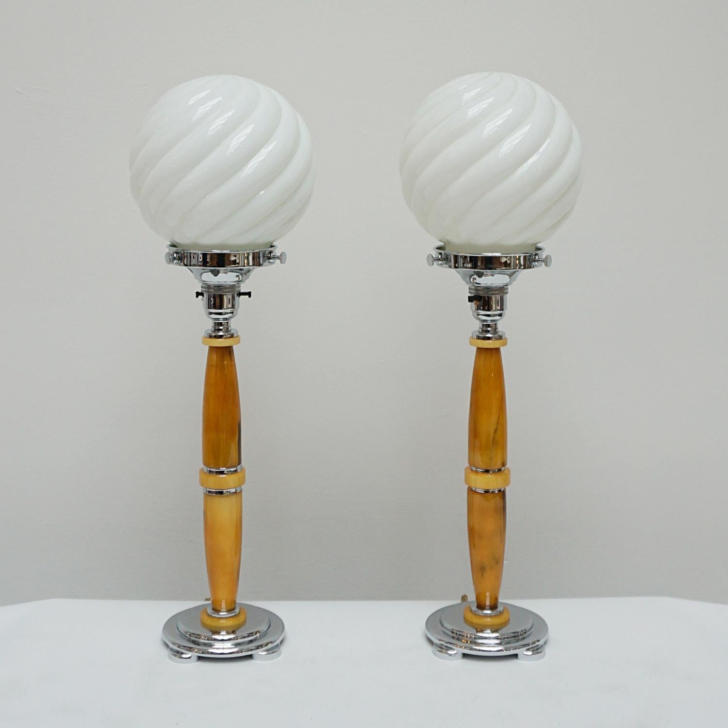 A pair of art deco table lamps. Marbled amber bakelite stem with chromed metal banding over a stepped circular chrome metal base. Beveled white glass shades. 

Dimensions: H 46cm D 10.5cm

Origin: English

 All of our lighting is fully