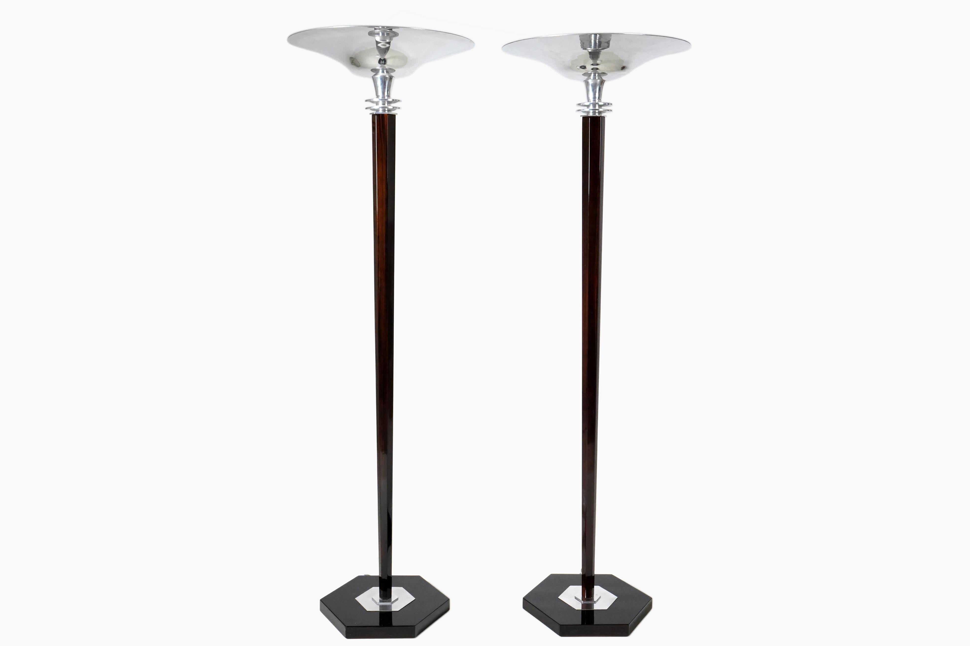 These dramatic torchieres were made in Budapest, Hungary according to authentic 1930s original designs. The shaft and base are poplar wood, covered in walnut veneer. The upward-flaring shade and other fittings are nickel-plated aluminum. During the