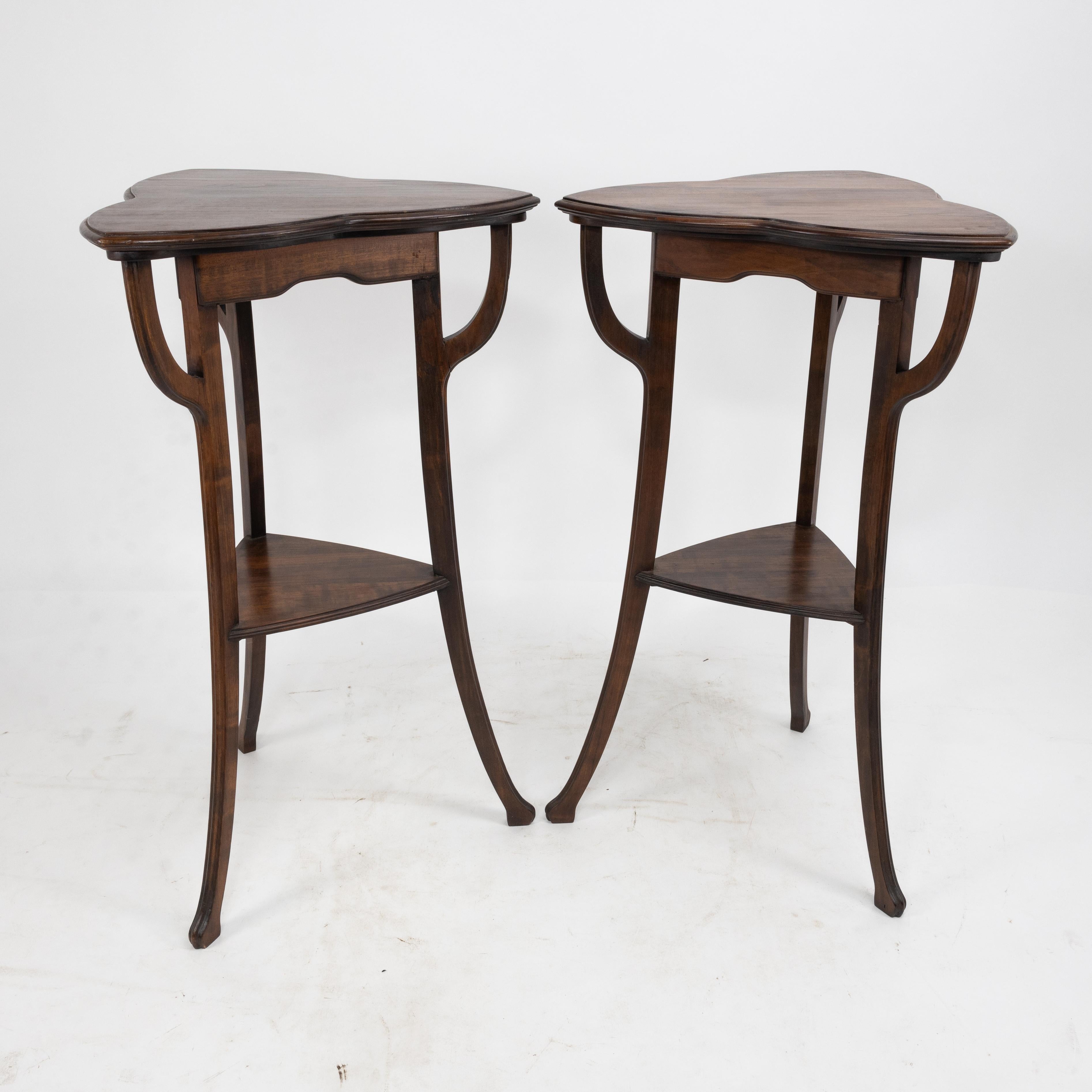 A pair of Art Nouveau beech stained side tables with clover leaf style tops supported with whiplash uprights beside shaped aprons, flowing with elegant legs finishing on little pad feet, united by a lower triangular shelf, with subtle astragal