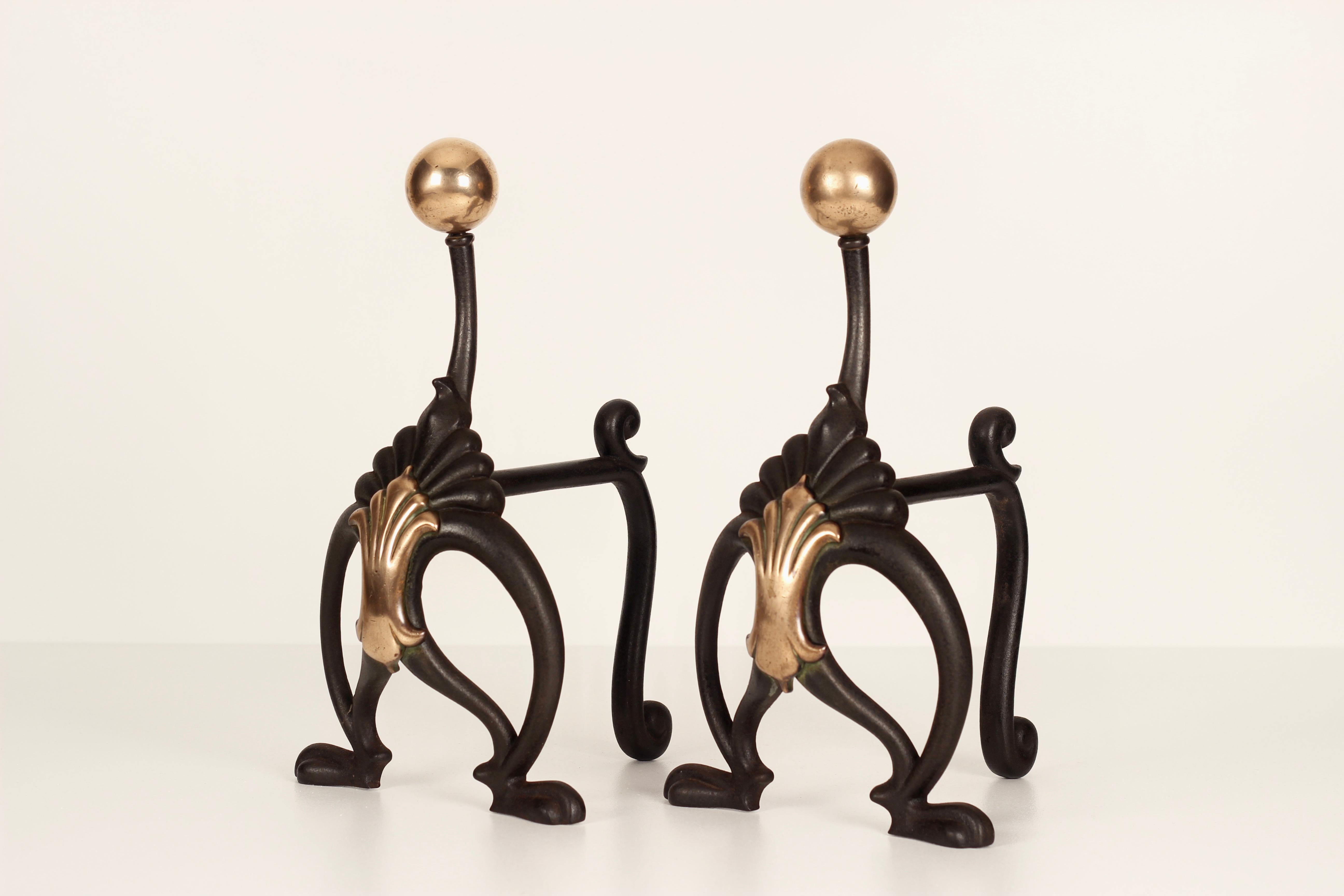 A pair of Art Nouveau fire dogs from the 1890-1910 period by the English maker WILLIAM TONKS & Sons. To us this pair resemble the stance of a bird or specifically a Peacock.
Made from Brass and iron, these fire dogs have copper roundels which