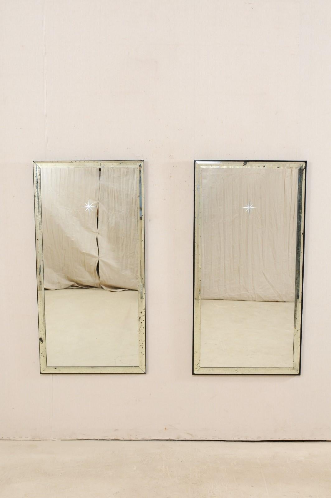 A pair of Artisan made mirrors with silver églomisé starbursts and antiqued mirror surround. This pair of rectangular-shaped mirrors stand just over 4 feet in height. They are artisan made with clean, antiqued-mirror surrounds, and a clear mirrored