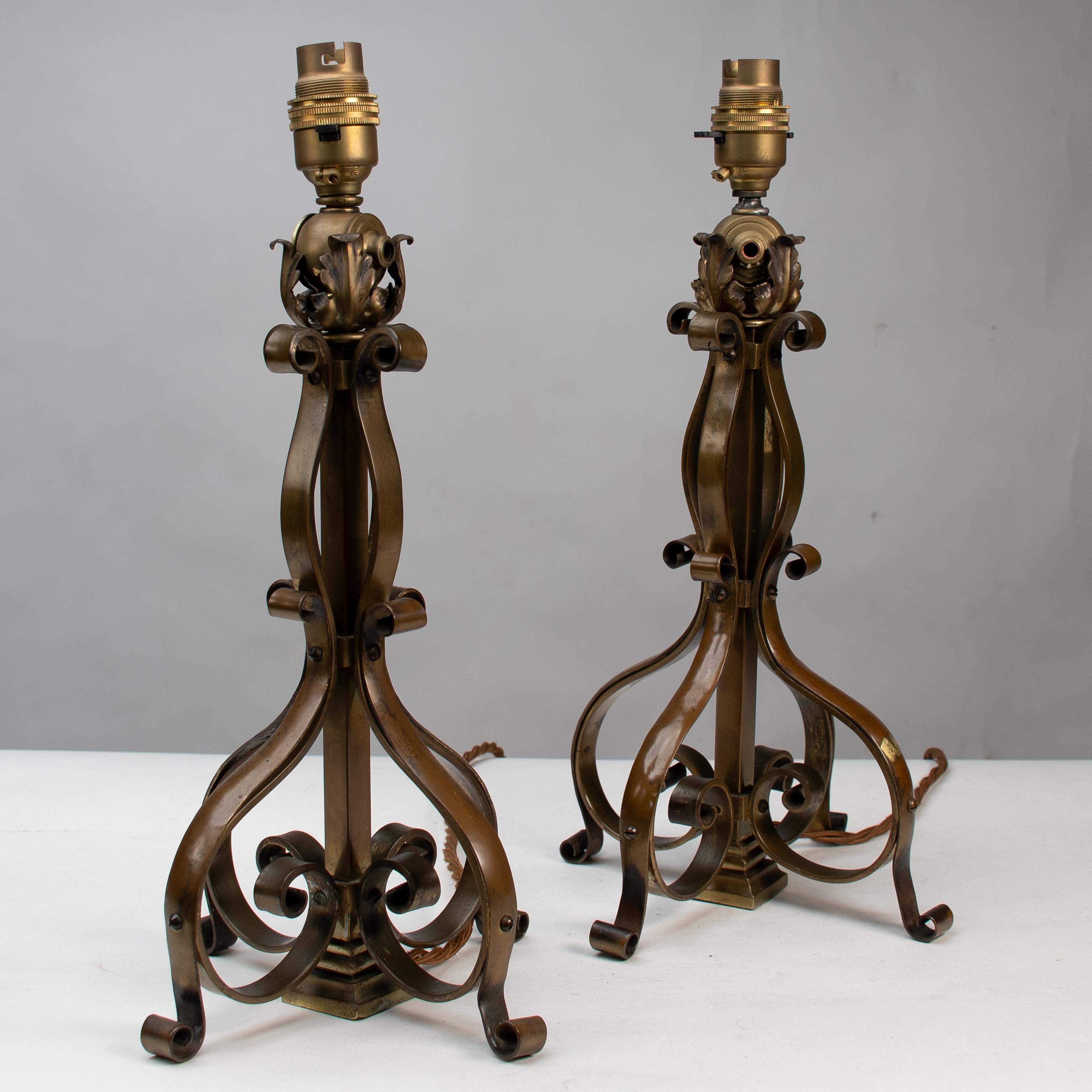 Pareja de lámparas de sobremesa o de poste de latón Arts and Crafts con decoración de volutas formadas a mano y decoración de hojas en la parte superior.