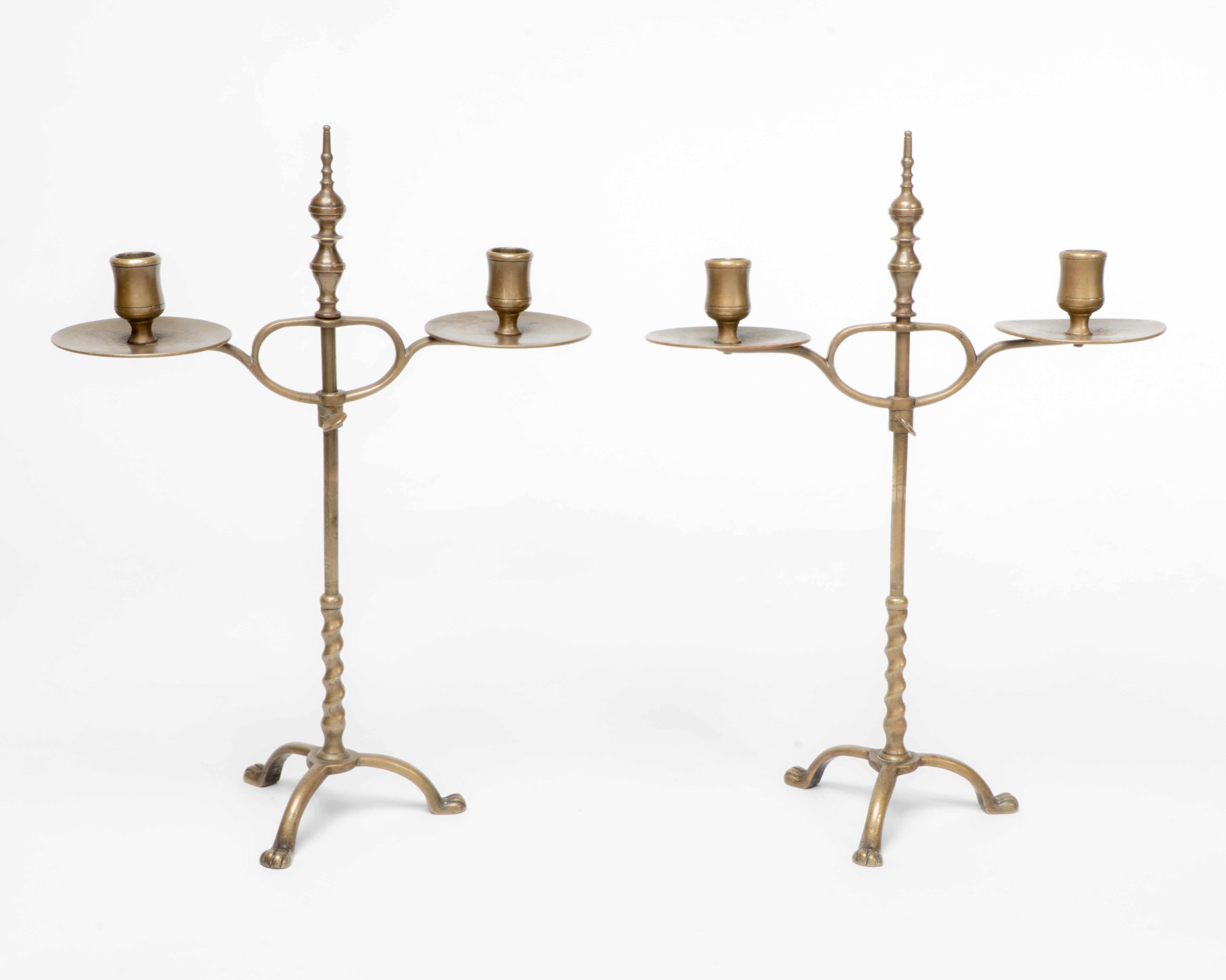 Coppia di candelabri a due rami in ottone di Arts and Crafts, regolabili in altezza e dotati di viti a testa zigrinata, con ampi vassoi raccogli gocce e un dettaglio di torsione d'orzo sul gambo inferiore che si ergeva ad arco e piedi a zampa nello