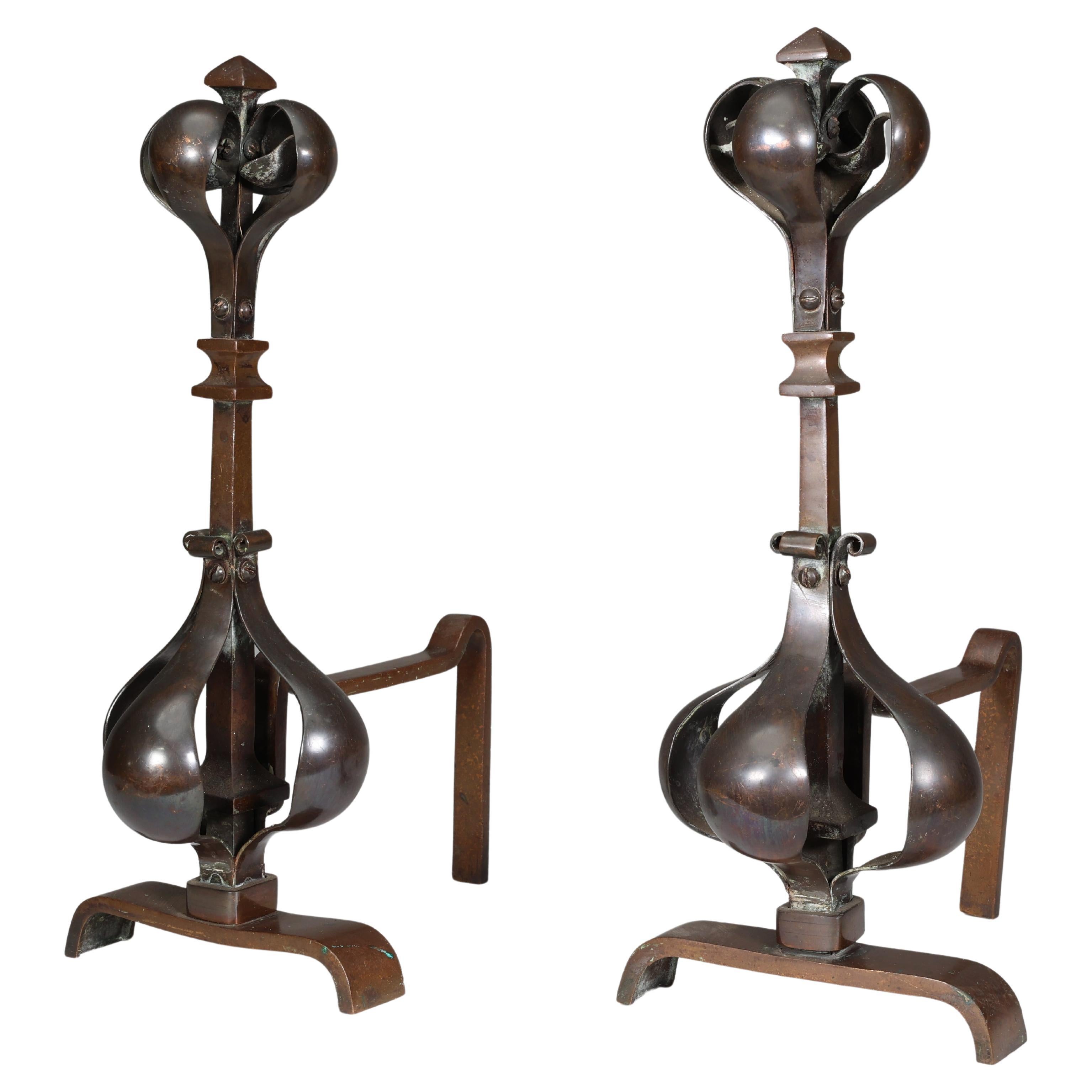 A pair of Arts and Crafts copper and bronze fire dogs with pyramid style finials