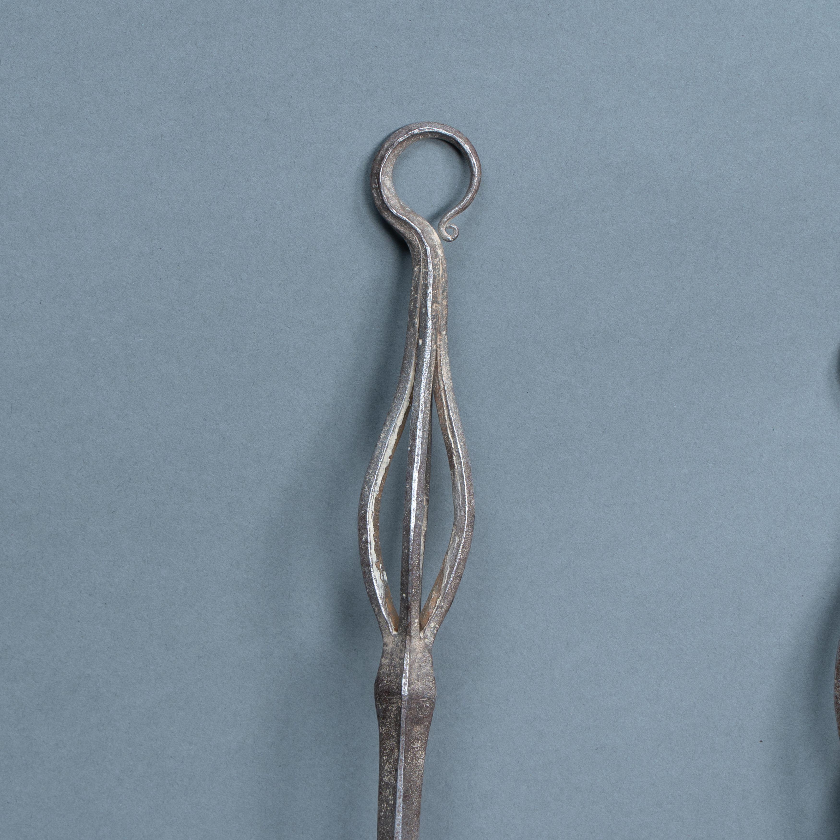 Coppia di utensili da fuoco in acciaio Decorative Crafts con piani circolari pendenti e piccole volute che li decorano, manici aperti martellati con spacco a scalpello. Consiste in un forchettone e in un attizzatoio.
Misure:
Vanga - Altezza: 58.5cm