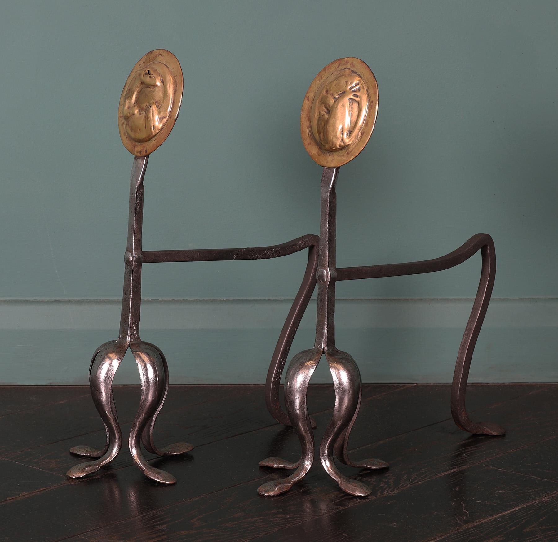 A pair of Arts & Crafts brass & wrought andiron rests. The brass discs with newt and frog central details supported on forged leaf feet. Restored. 
Circa 1880