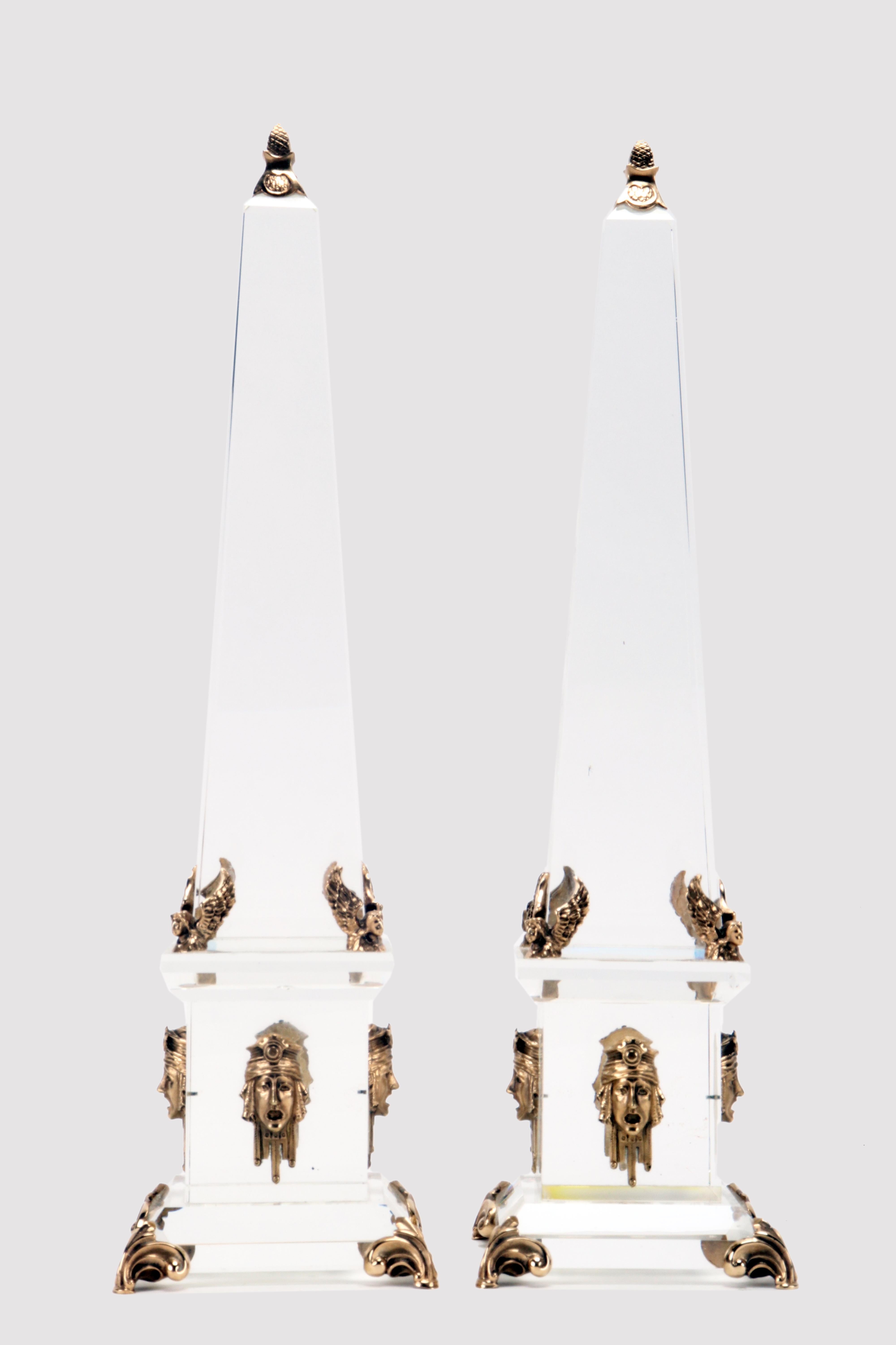 A pair of Grand Tour obelisks. Made of Baccarat crystal. The plinth rests on 4 legs in gilded bronze in the shape of a paw, 4 angel heads, also made of gilded bronze, separate the obelisk from the base. At the center of the sides of the plinth,