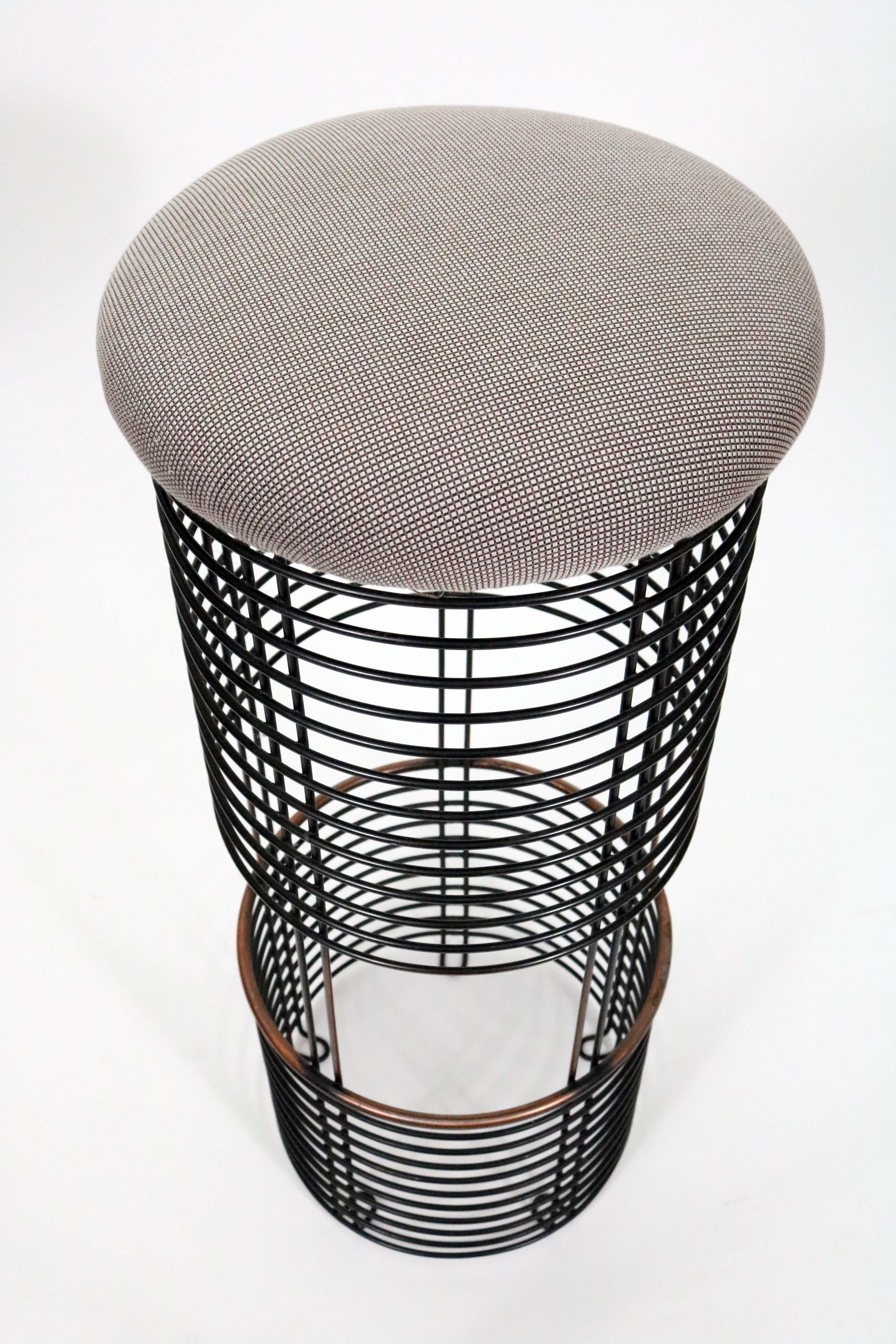 A beautiful and intriguing pair of rare bar stools by Verner Panton. 

A comfortable grey/taupe upholstered seat sits atop a black enameled iron base with a copper footrest.

 
