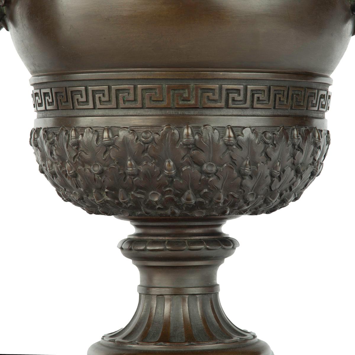 A pair of Belgian bronze urns by Luppens, Brussels, each in the form of a classical two-handled vase, decorated in high relief with bands of acorns on dense foliage, Greek key pattern and scrolls with shells, the handles comprising double headed