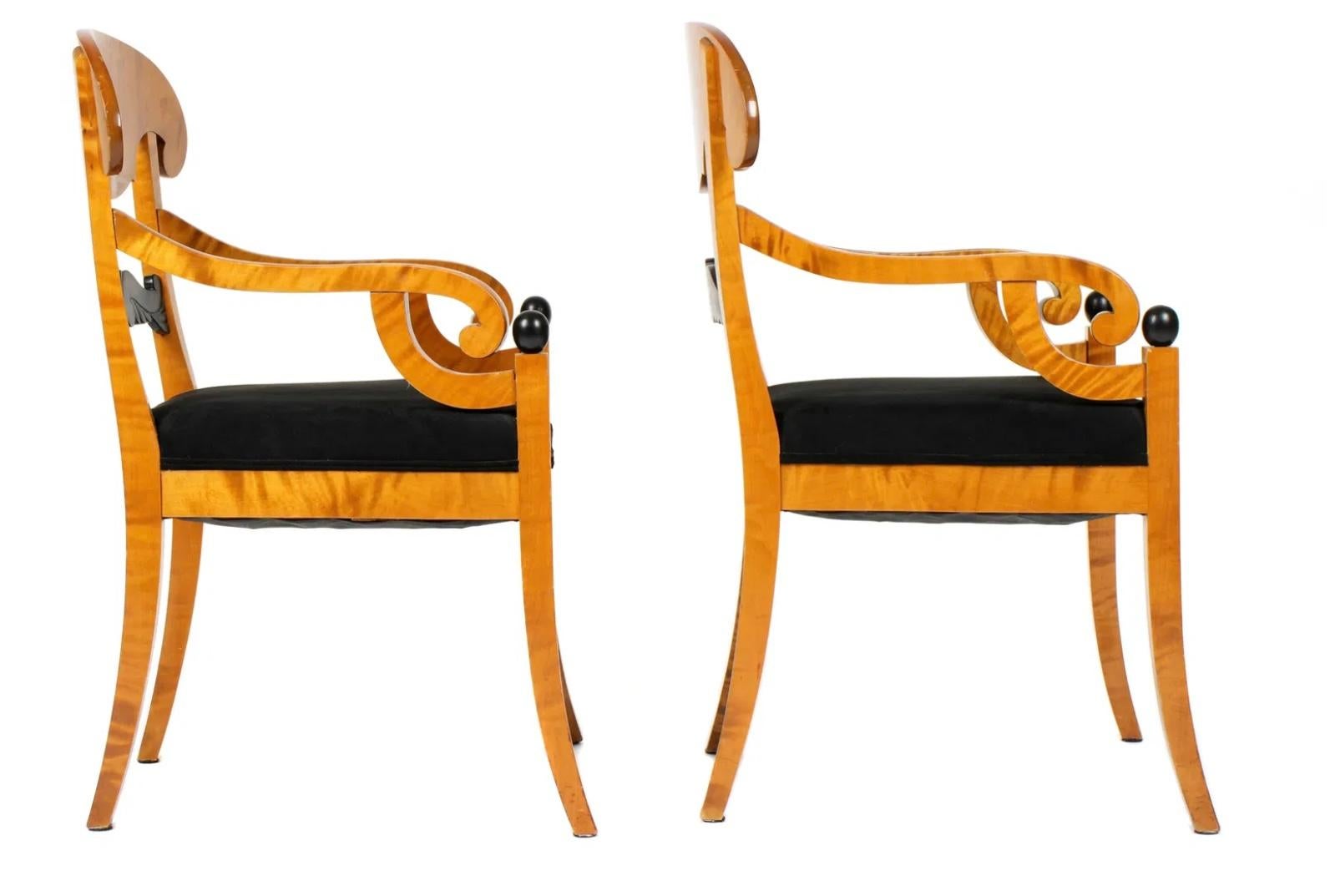 Pareja de sillones estilo Biedermeier. Las sillas tienen armazón de abedul, barandilla superior perfilada sobre respaldo tallado ebonizado, brazos acabados en asideros de volutas, remates de bolas negras ebonizadas. Las sillas descansan sobre patas