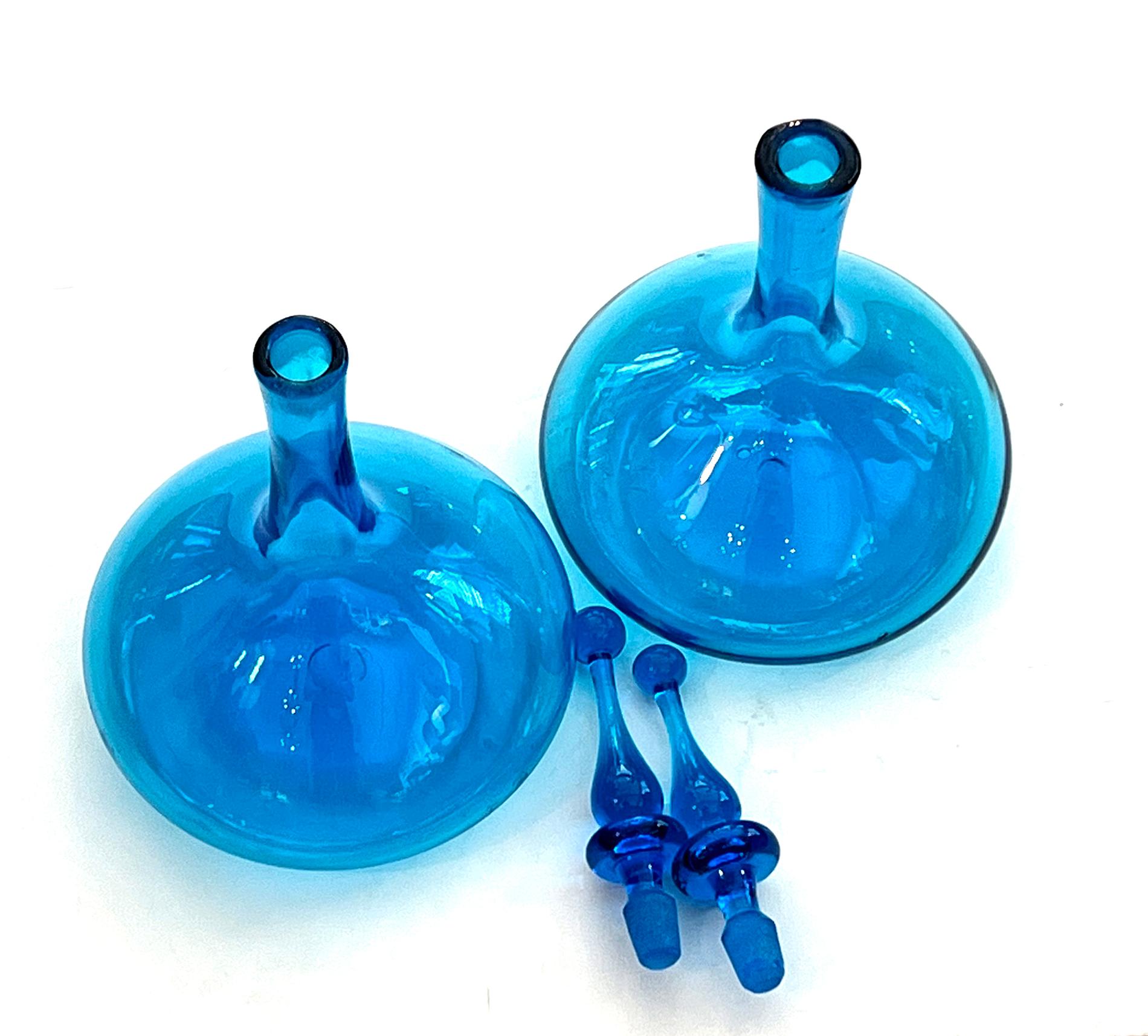 A good example of Blenko hand-blown glass, each with long neck above a bulbous body fitted with a water-drop solid glass stopper all in a cerulean blue clear glass; with pontil marks to underside; crafted using the Venetian free-blown glass