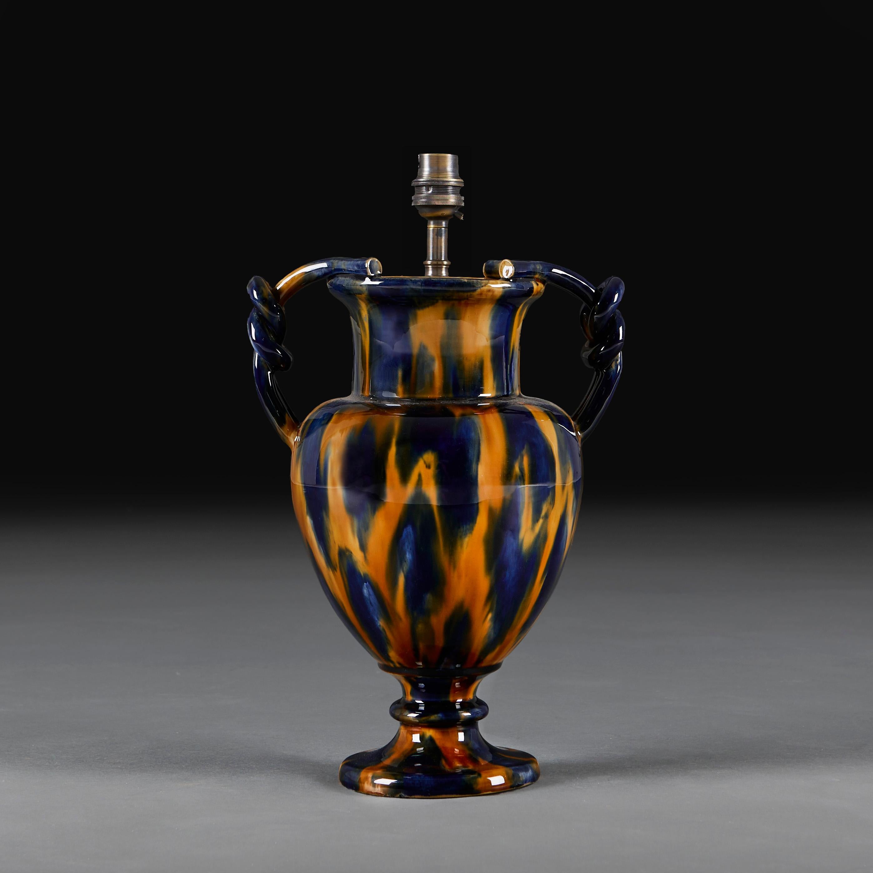 France, circa 1920
An unusual pair of early twentieth century aptware vases of amphora form and plaited handles to the necks, supported on circular plinth bases, with amber and blue glaze throughout. 

Height of vase            32.00cm
Height with